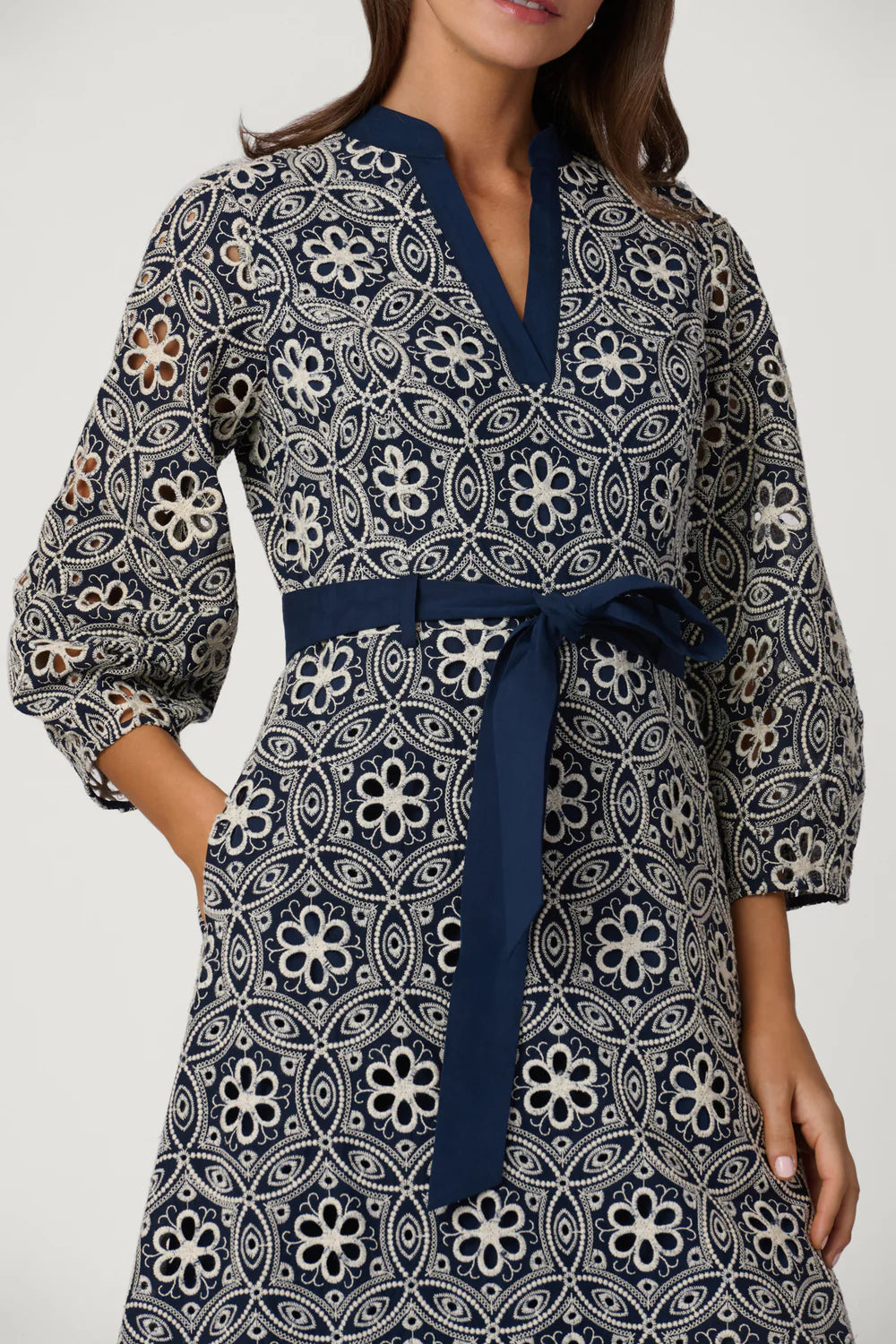 Woman wearing a patterned dress with a blue belt against a white background