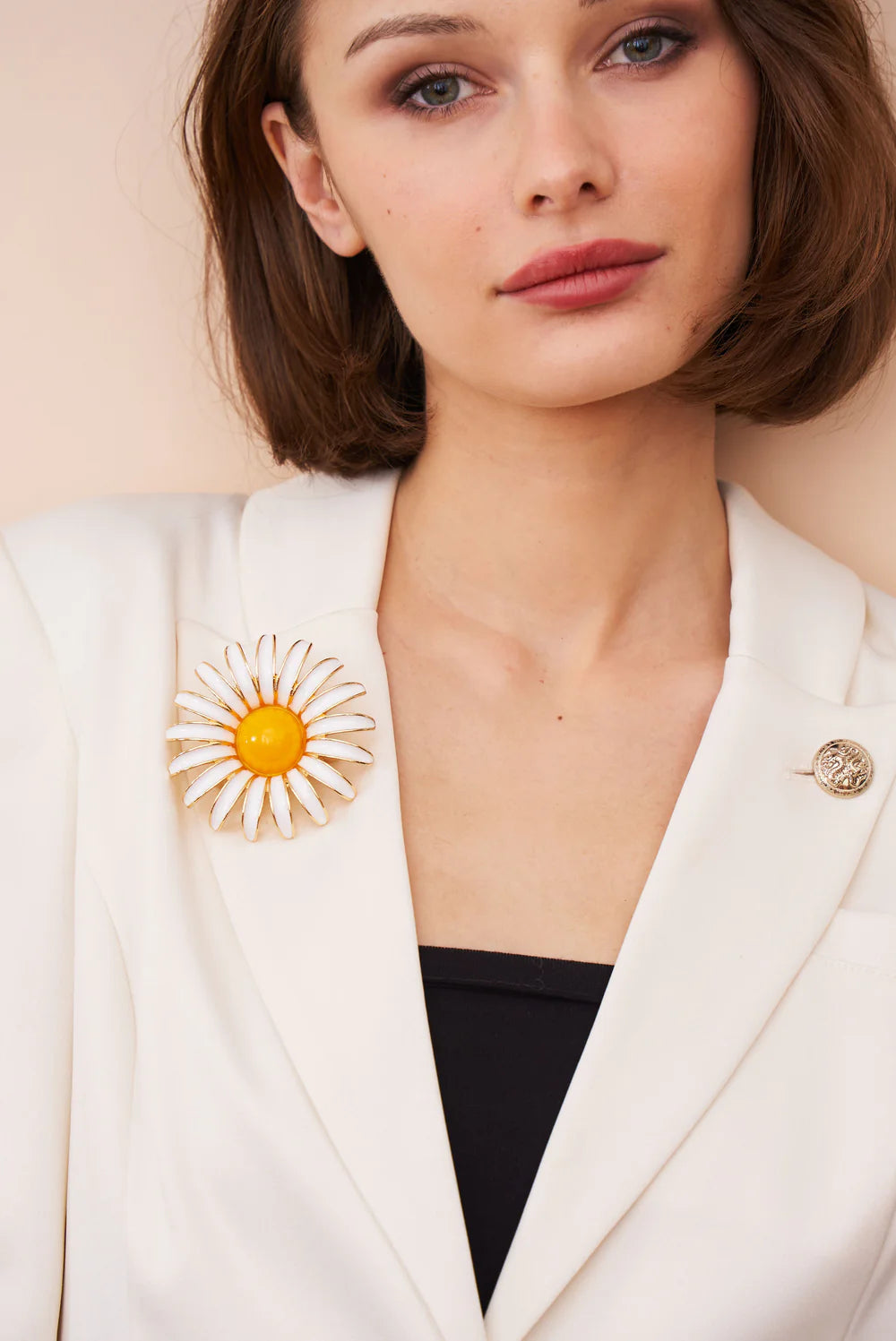 Woman wearing a white blazer with a sunflower brooch against a beige background