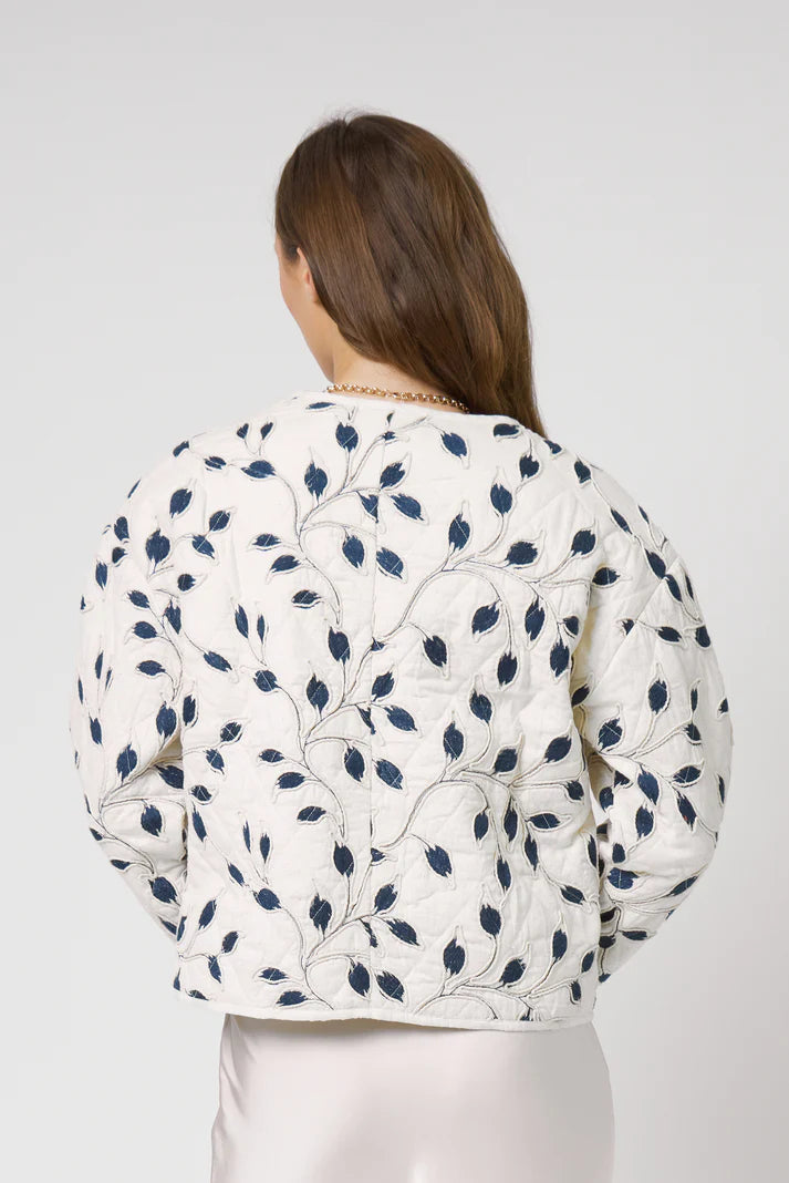 Woman wearing a white floral patterned jacket on a plain background