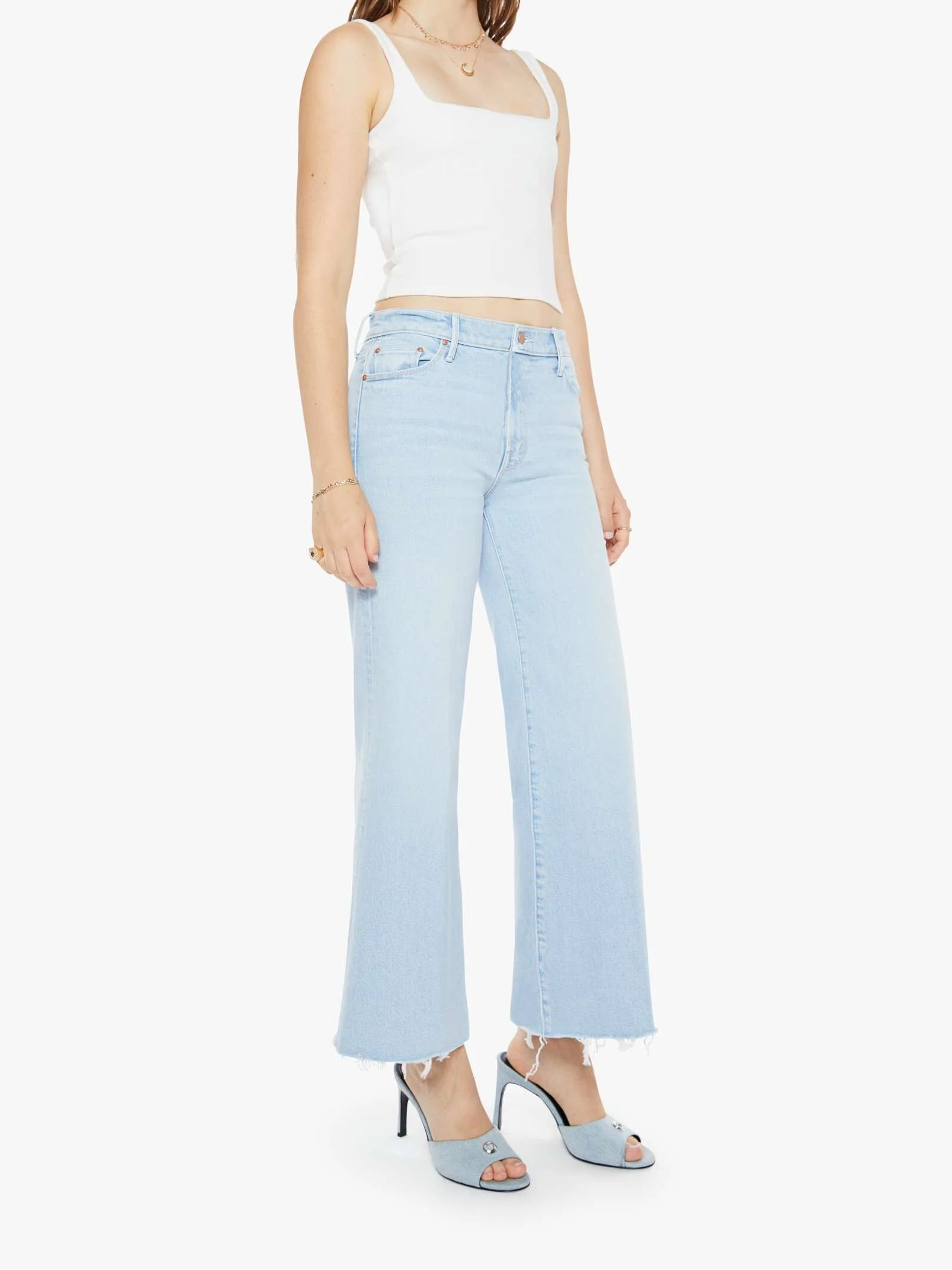 A female model wearing high-rise ankle fray jeans with a flared wide leg and a white tank top.