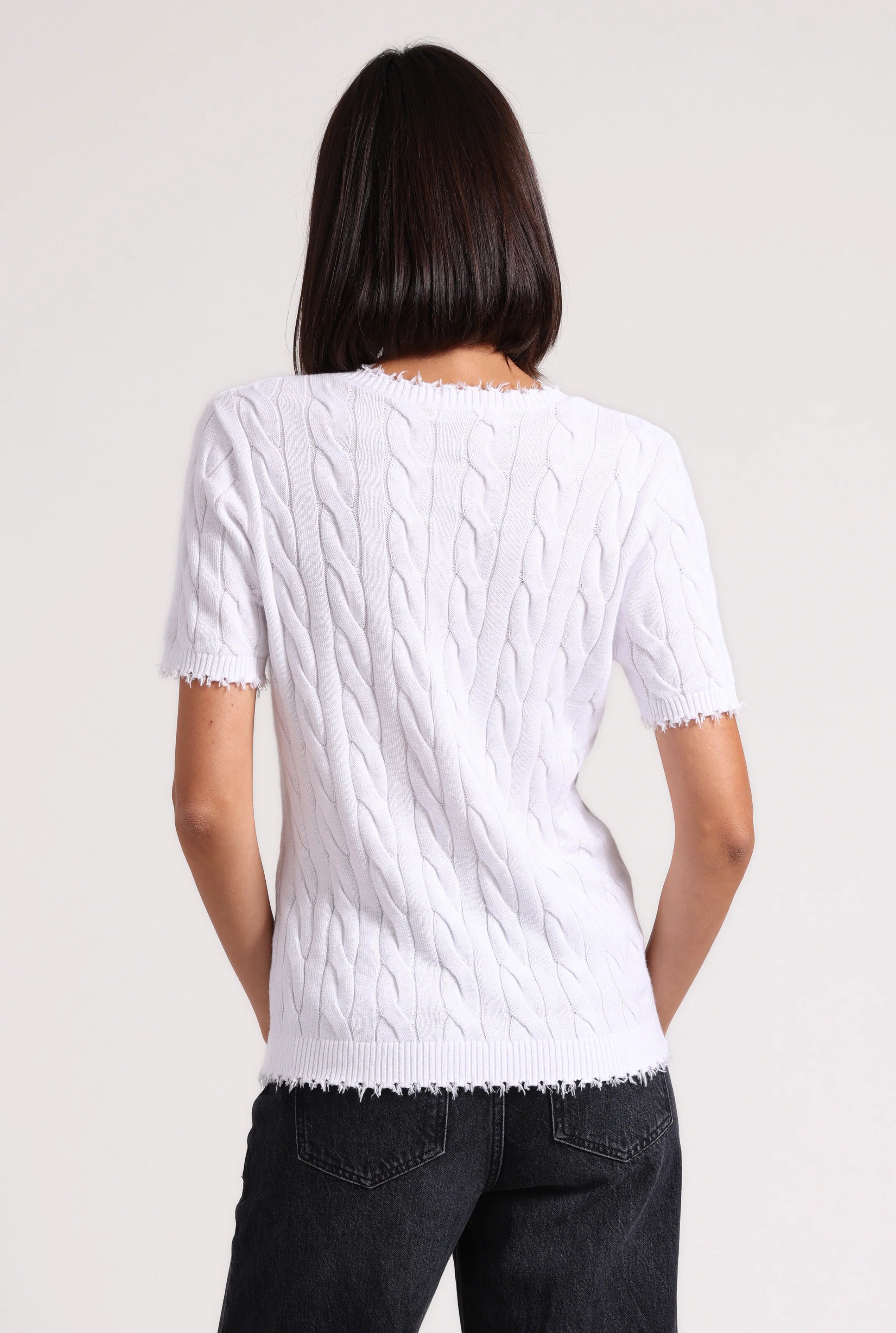 Person wearing a white cable knit sweater on a plain background