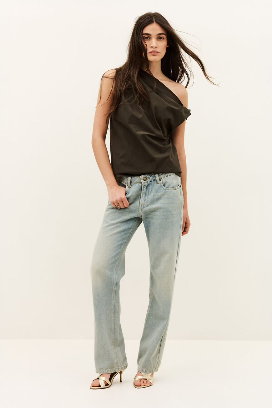 Woman wearing a dark green one-shoulder top and light blue jeans on a white background