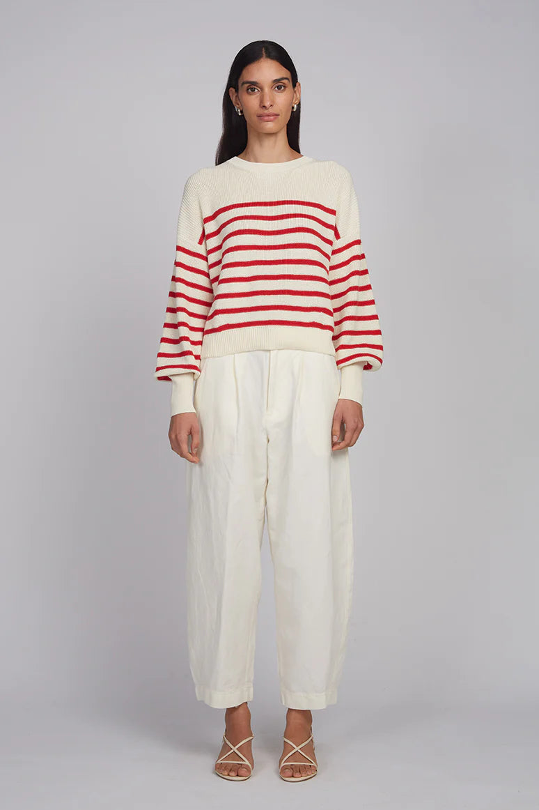 Woman wearing a red and white striped sweater and white pants on a gray background