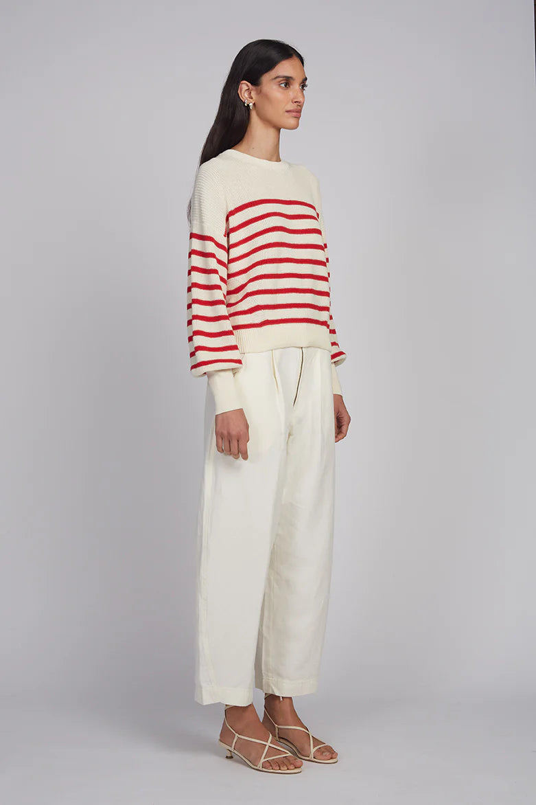 Woman wearing a red and white striped sweater with cream pants on a gray background