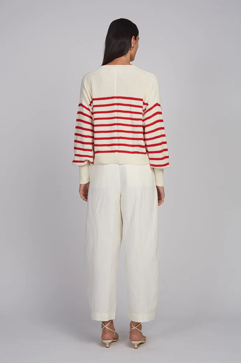 Person wearing a red and white striped sweater with white pants on a plain background