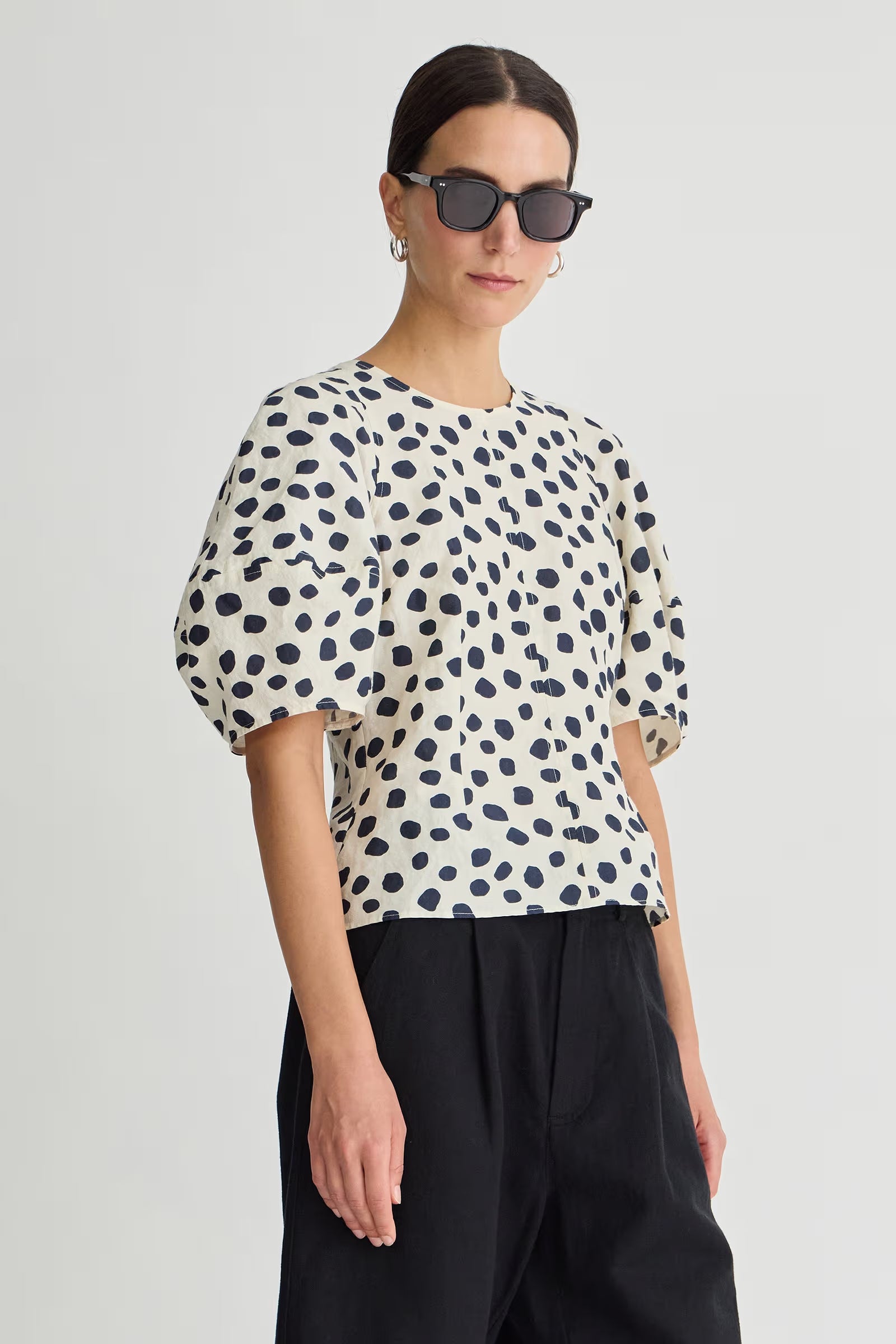 Woman wearing a polka dot blouse and black pants on a light gray background