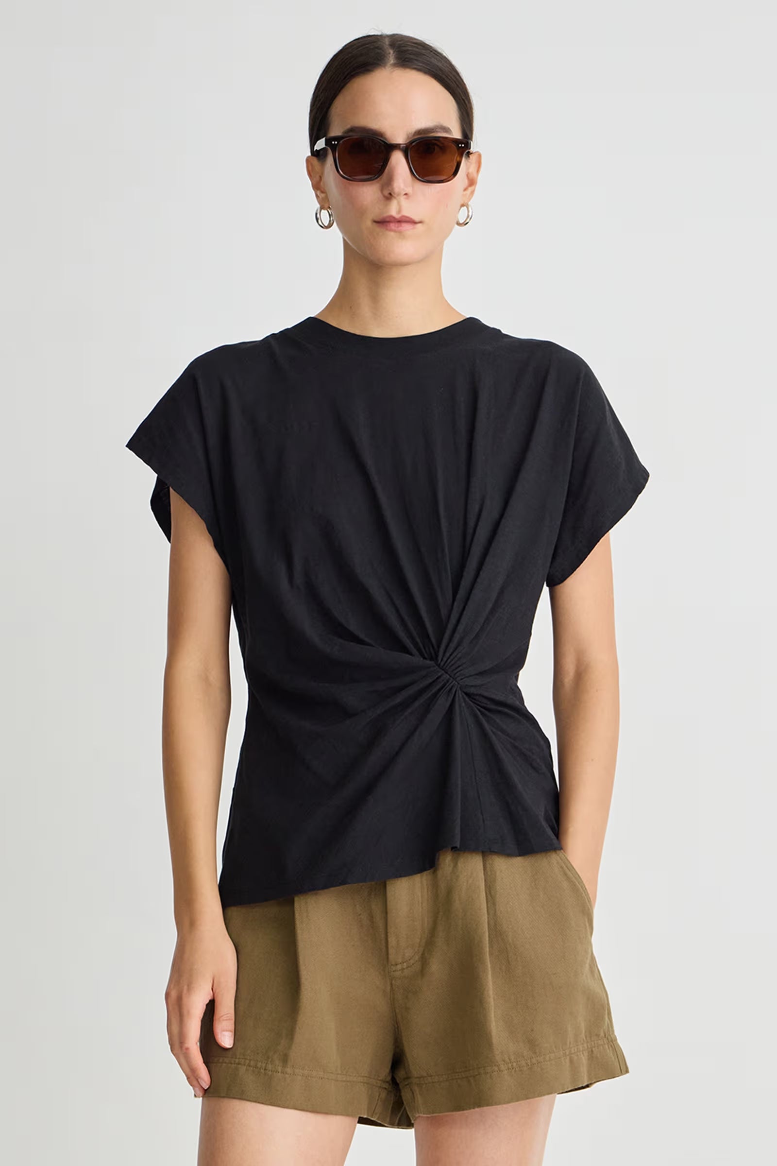 Woman wearing a black top with a knot detail and green shorts on a white background