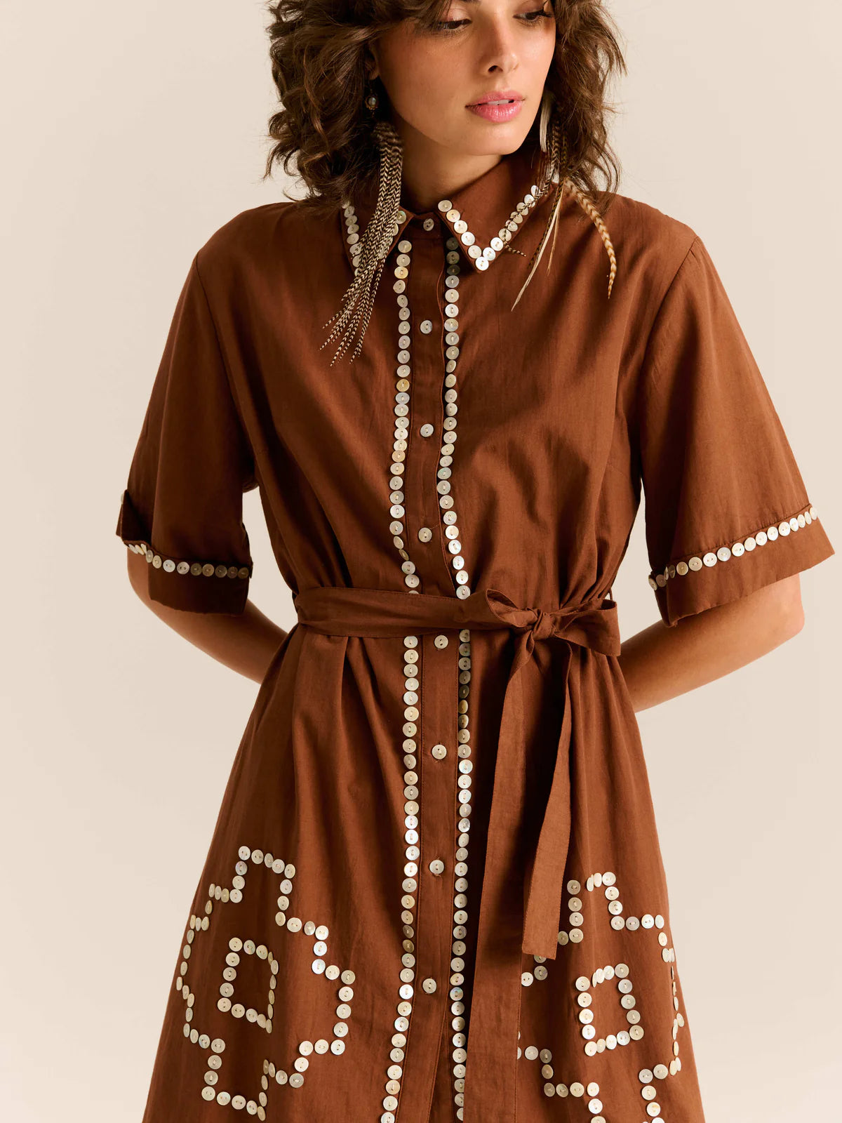 Woman wearing a brown dress with decorative buttons on a beige background