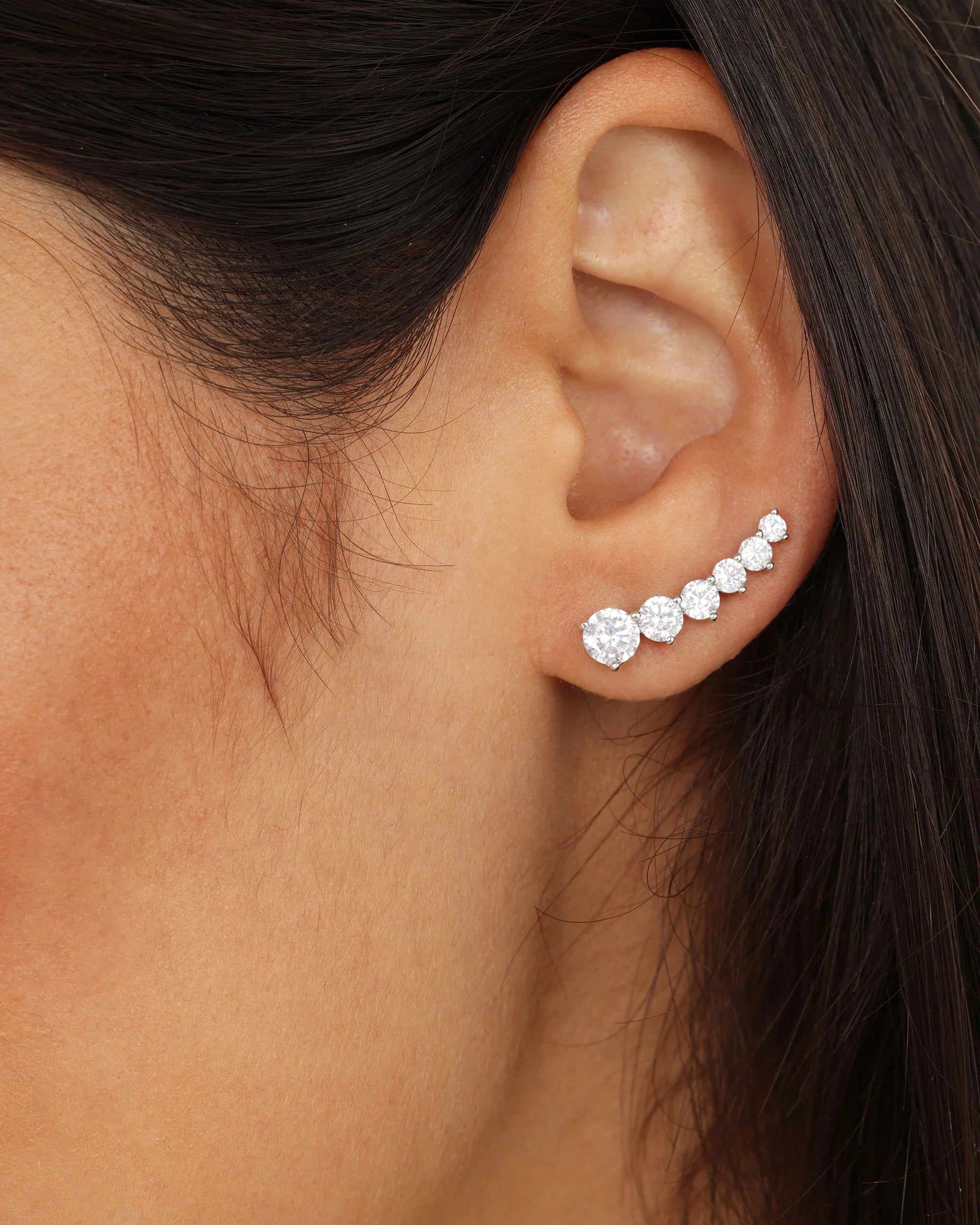 A close-up of a woman's ear wearing a curved row of sparkling diamond stud earrings in a silver setting.