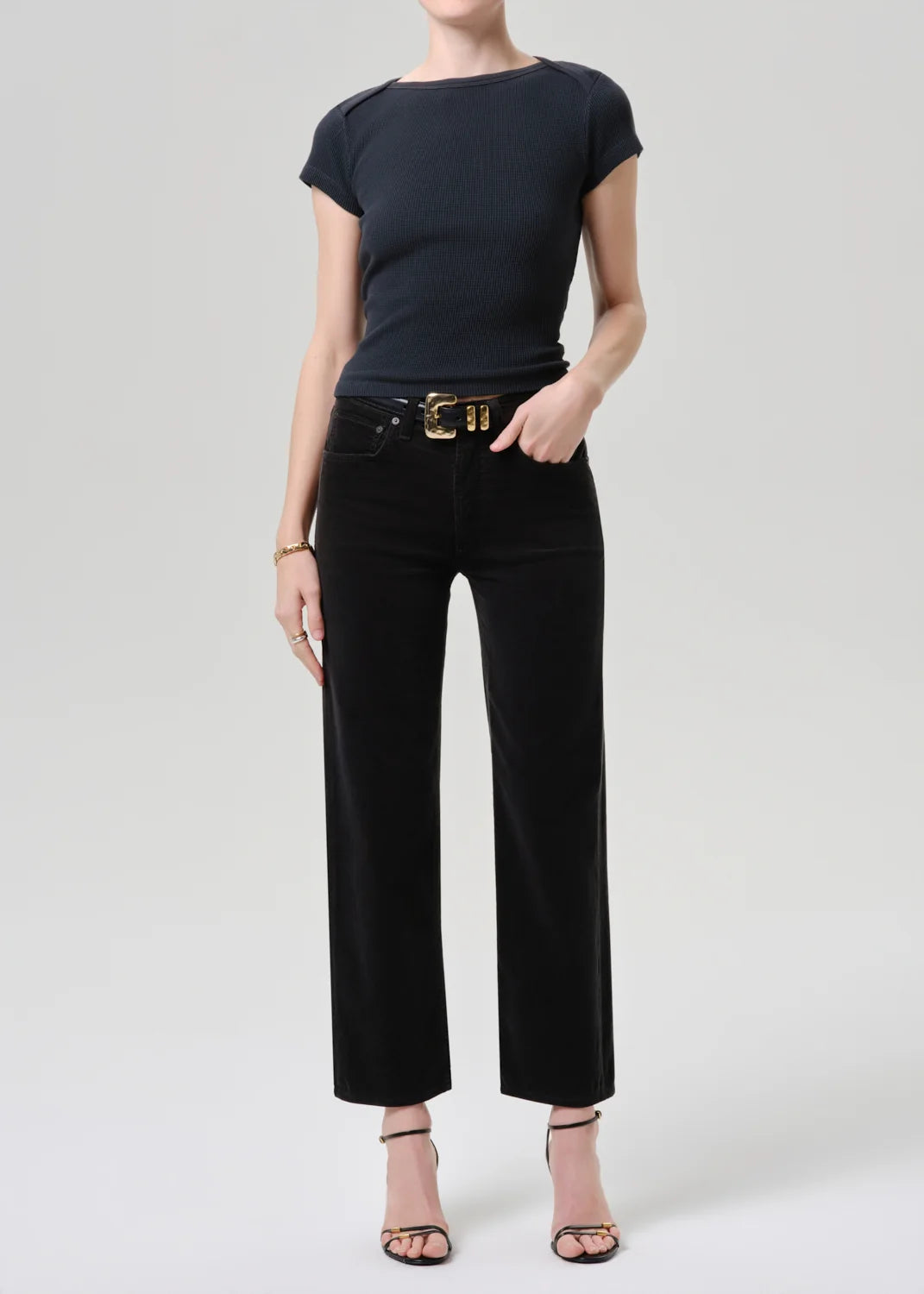 Person wearing a black t-shirt and black pants with a gold belt on a white background