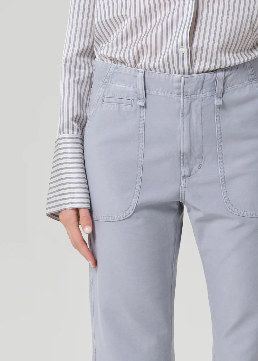 Person wearing light gray pants and a striped shirt on a plain background