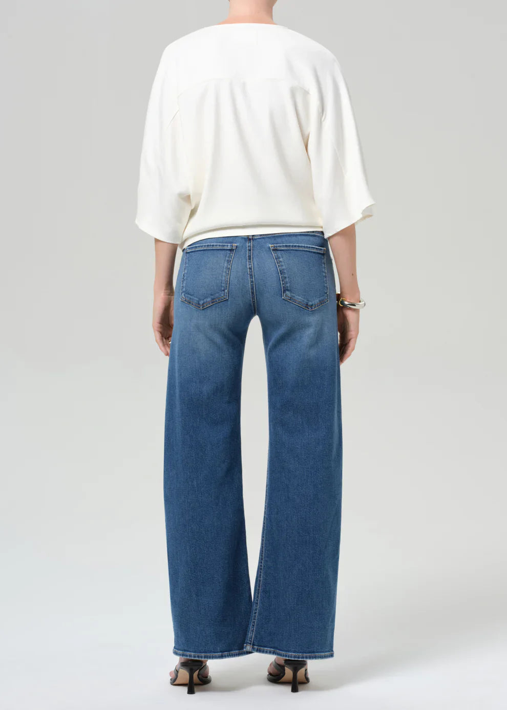 Person wearing a white top and blue jeans on a plain background