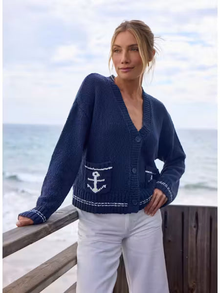 Woman wearing a navy blue cardigan with an anchor design by the ocean.