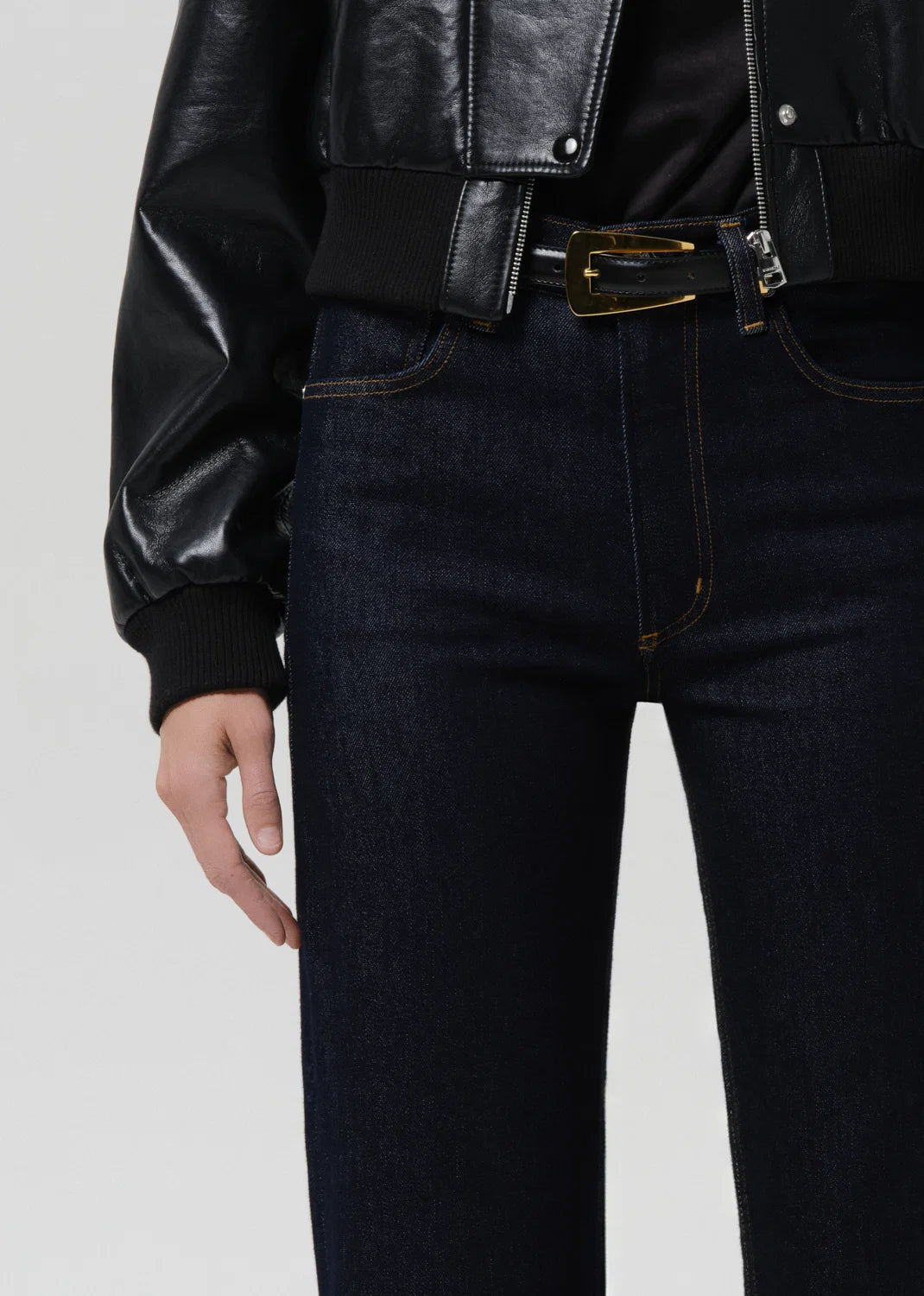 Person wearing a black leather jacket and dark jeans on a light gray background