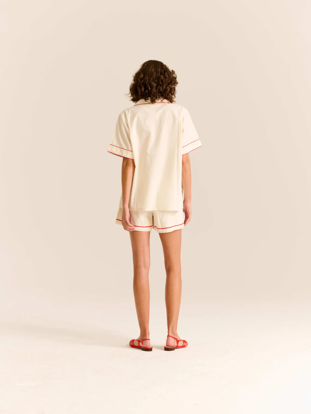 Person wearing a cream-colored pajama set with red trim on a beige background