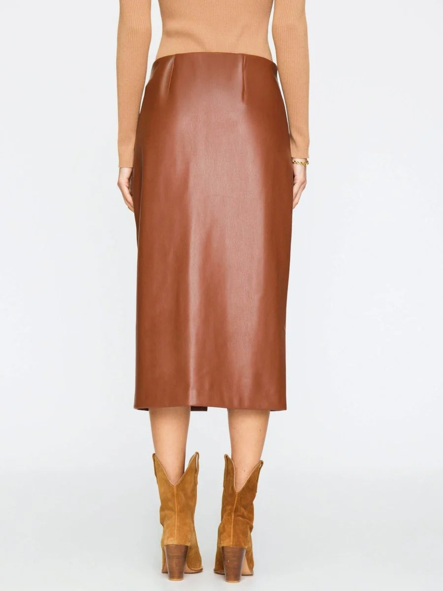 A model shown from the back wearing a brown faux-leather midi skirt, a beige top, and tan cowboy boots against a plain white studio background.