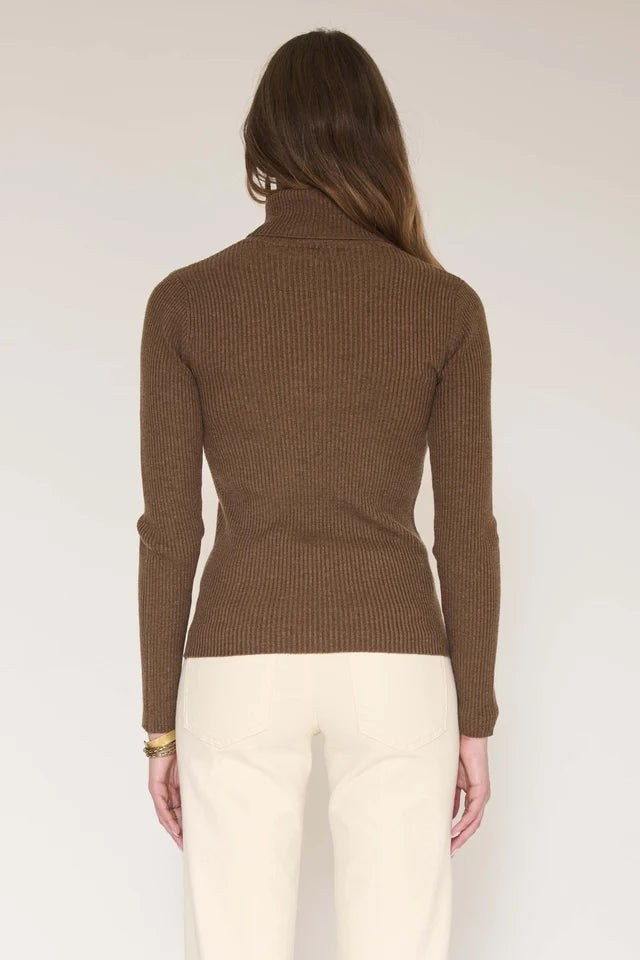A woman shown from the back wearing a ribbed brown mock neck sweater and cream pants against a plain light background.