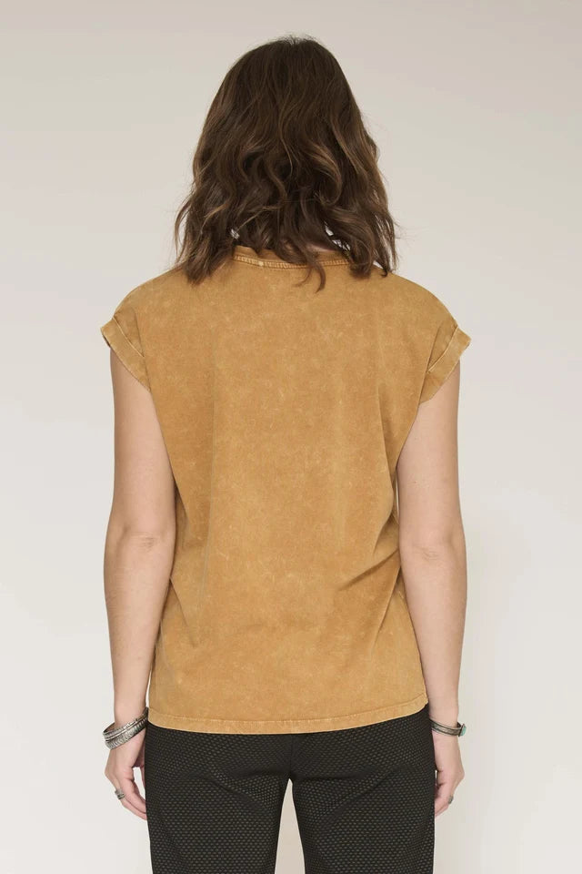 A woman viewed from the back wearing a cropped, short-sleeve mustard yellow top and black patterned pants against a plain light background.