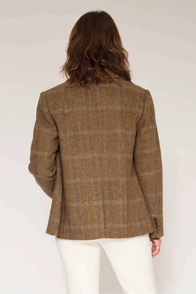 A woman viewed from the back wearing a brown plaid blazer and white pants against a plain light background.