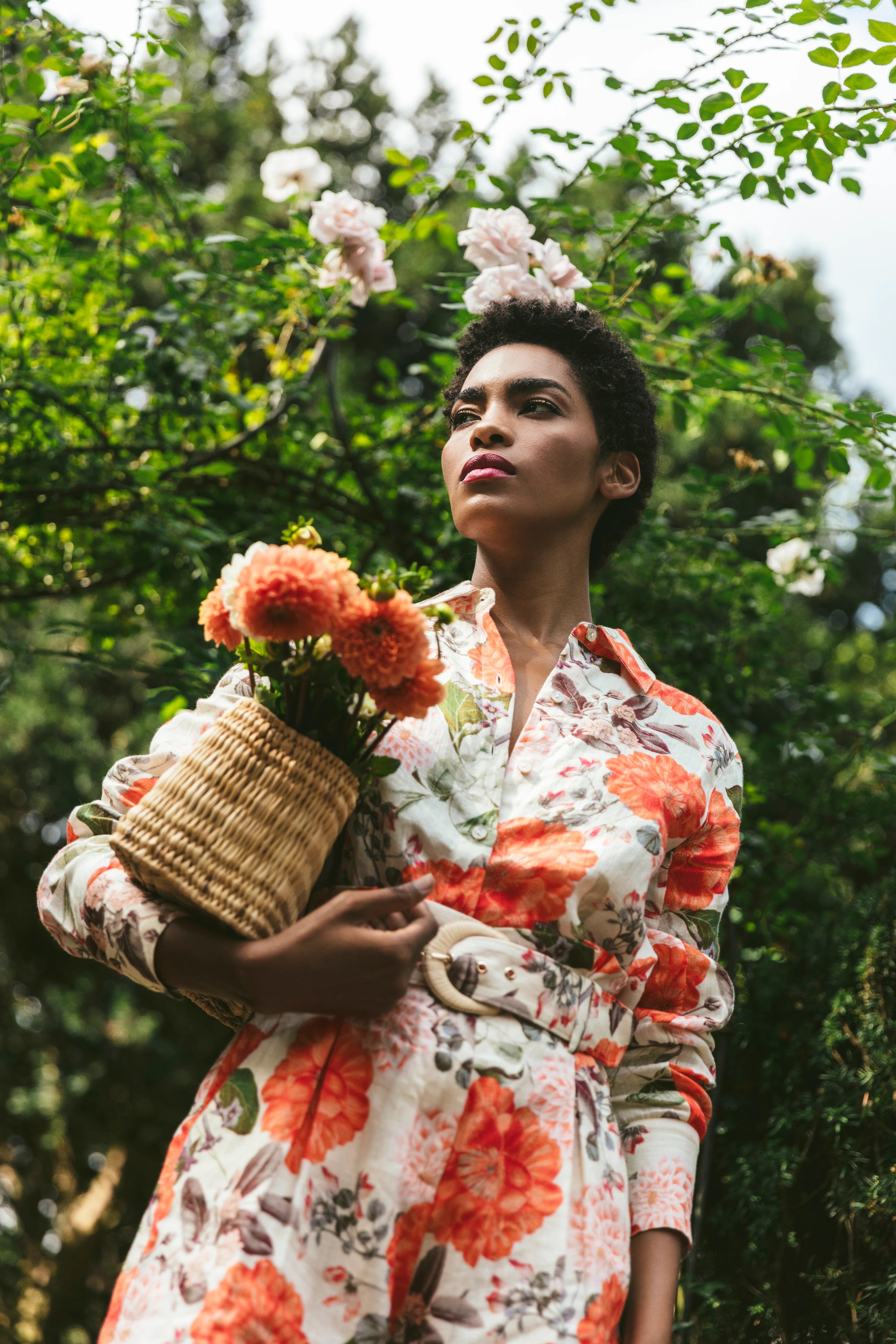 Woman in a floral dress holding flowers and a basket in a garden setting