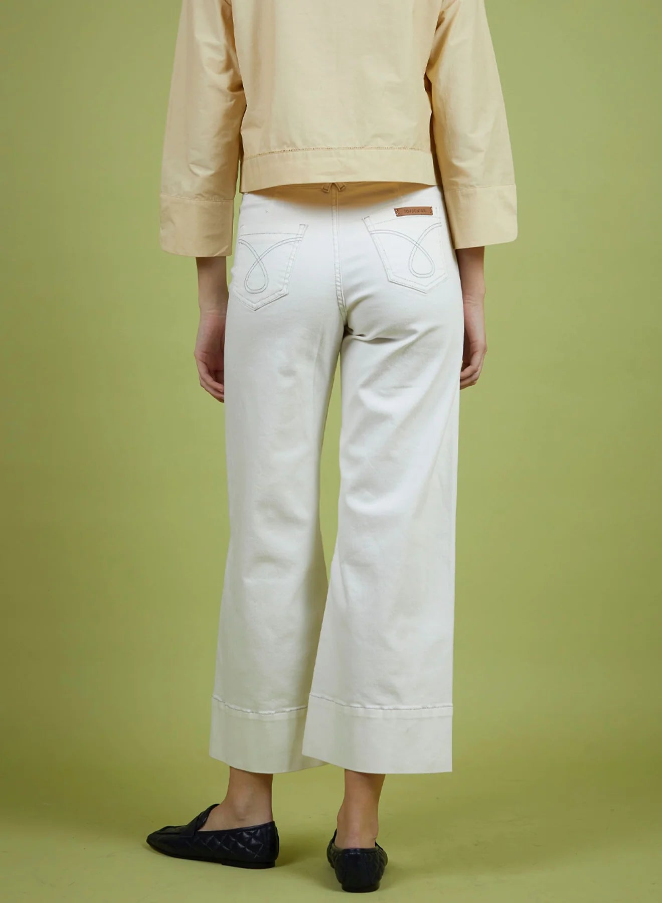 Person wearing a beige jacket and white pants on a green background