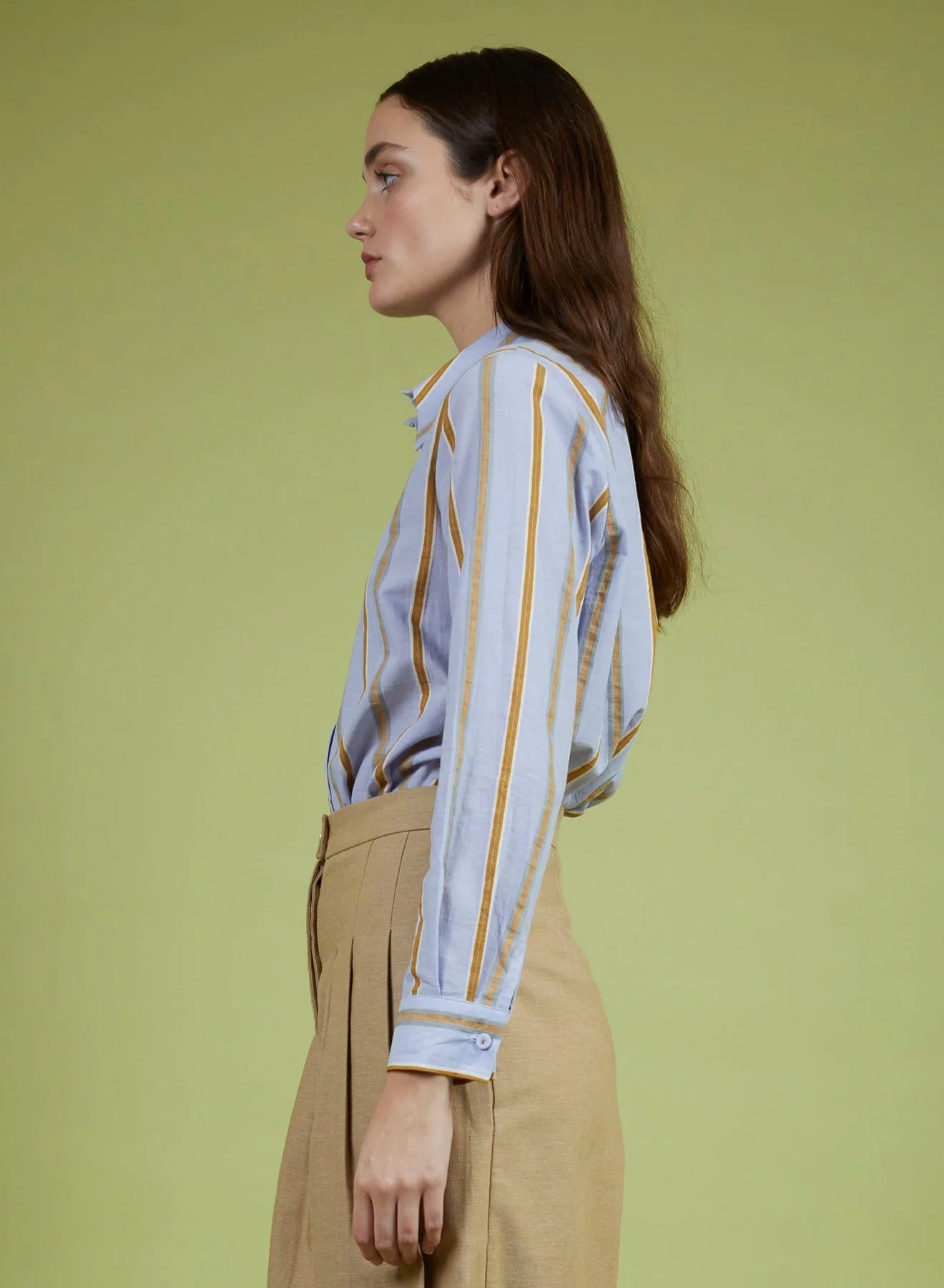 Woman wearing a patterned shirt and beige pants against a green background
