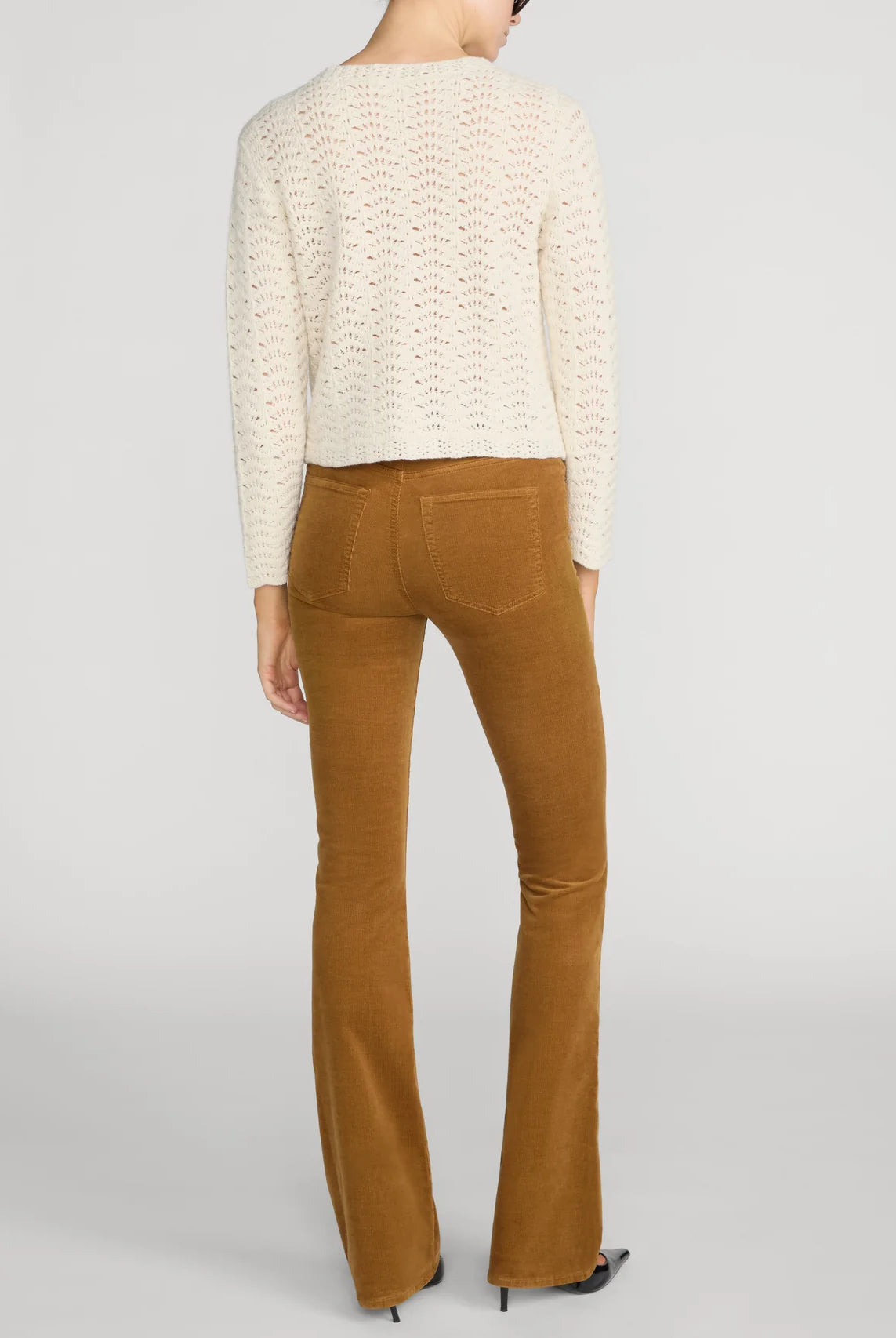 A model shown from the back wearing a cream-colored textured knit sweater and brown flared pants, set against a plain light gray studio background.