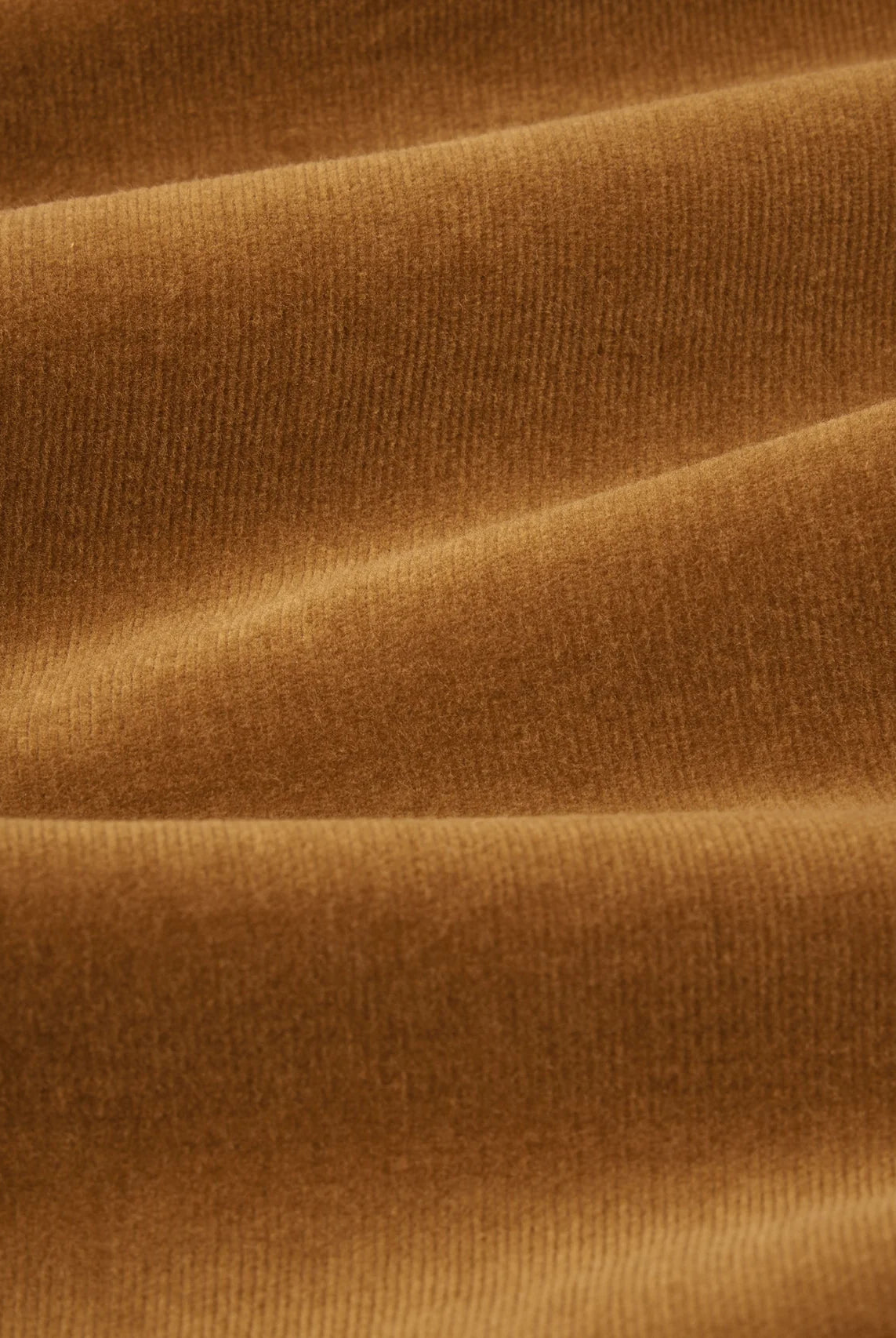 A close-up of draped ribbed fabric in a warm camel brown color, showing the texture and soft folds.