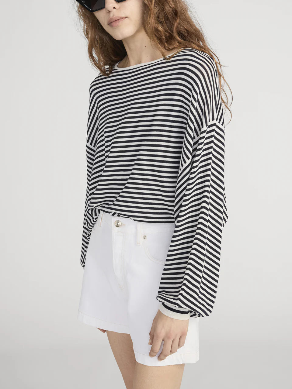 Person wearing a black and white striped long-sleeve top and white shorts on a light gray background