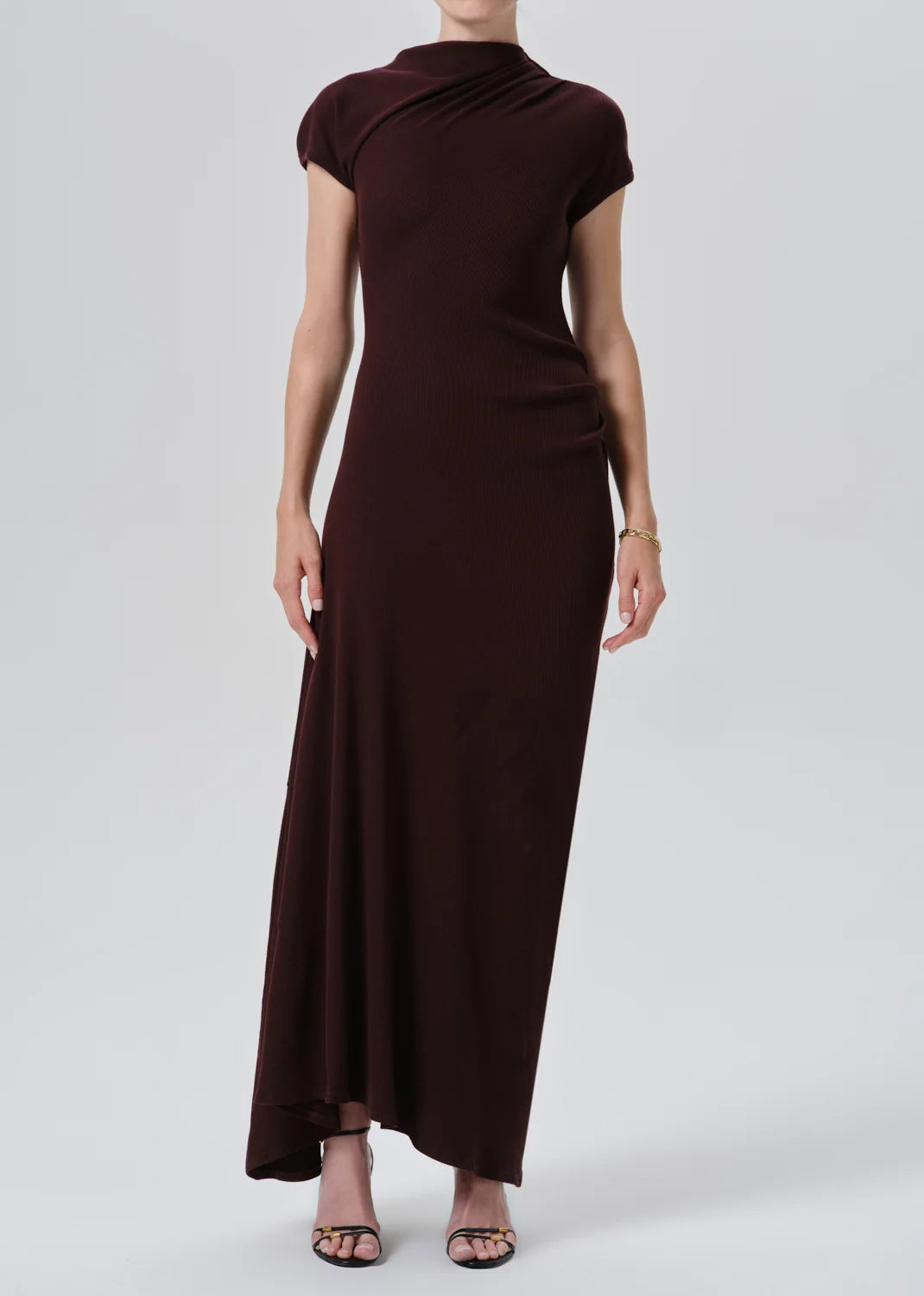 A woman modeling a dark brown, knee-length dress with a draped mock neck and short cap sleeves, shown from the back against a light gray studio background.