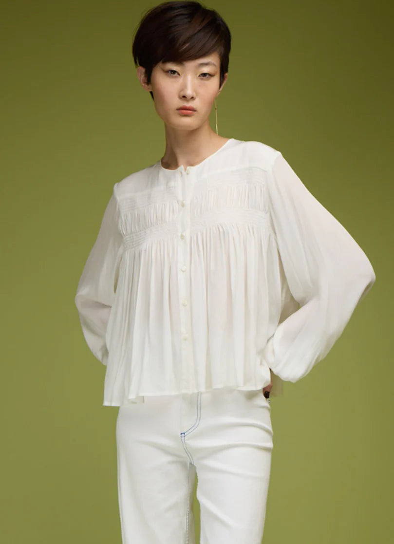 Person wearing a white blouse and pants against a green background
