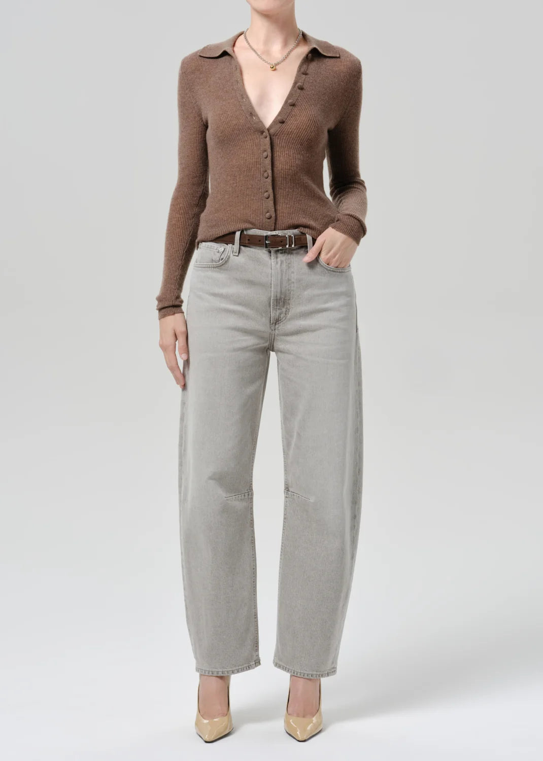 A model wearing a brown button-up knit cardigan, light gray wide-leg jeans, a dark brown belt, and beige pointed-toe heels, photographed against a light gray studio background.