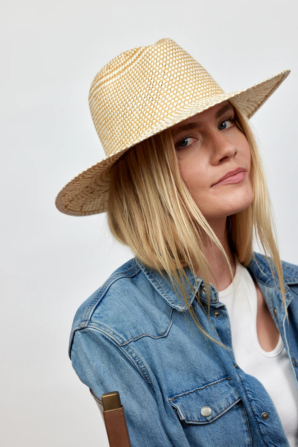 Woman wearing a straw hat and denim jacket on a plain background