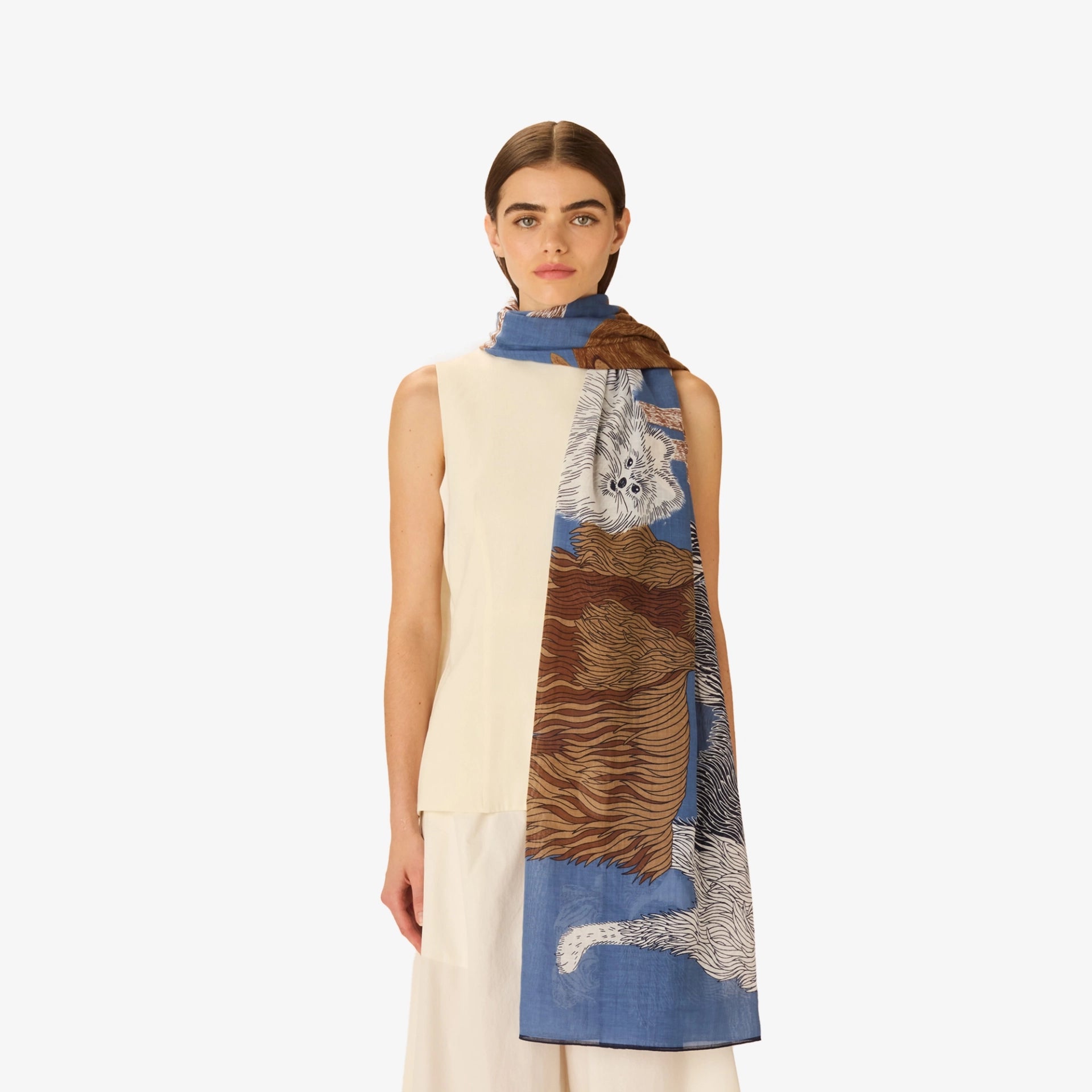 Woman wearing a sleeveless cream dress with a patterned scarf draped over her shoulders against a white background