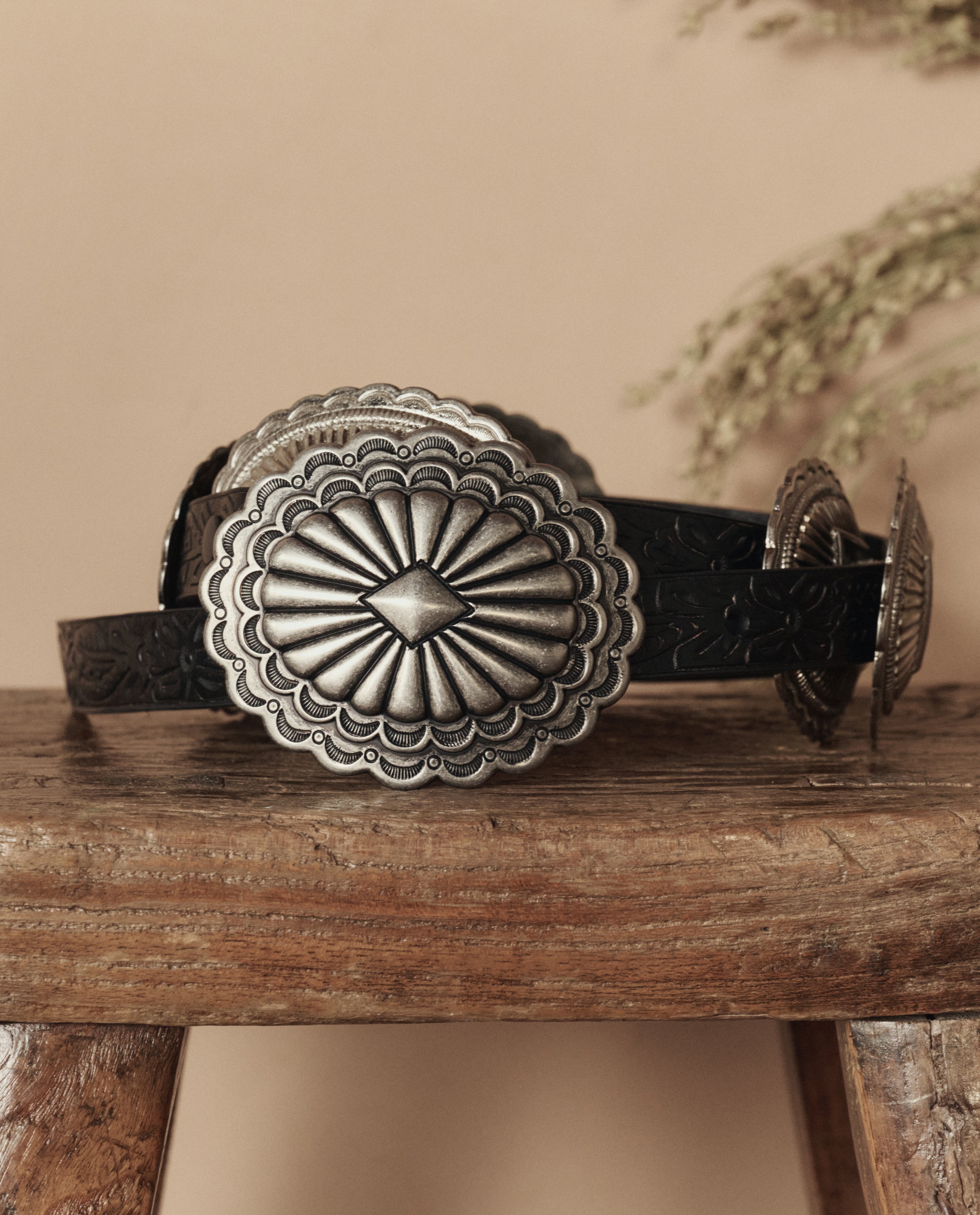 Black leather belt with silver concho on a wooden surface