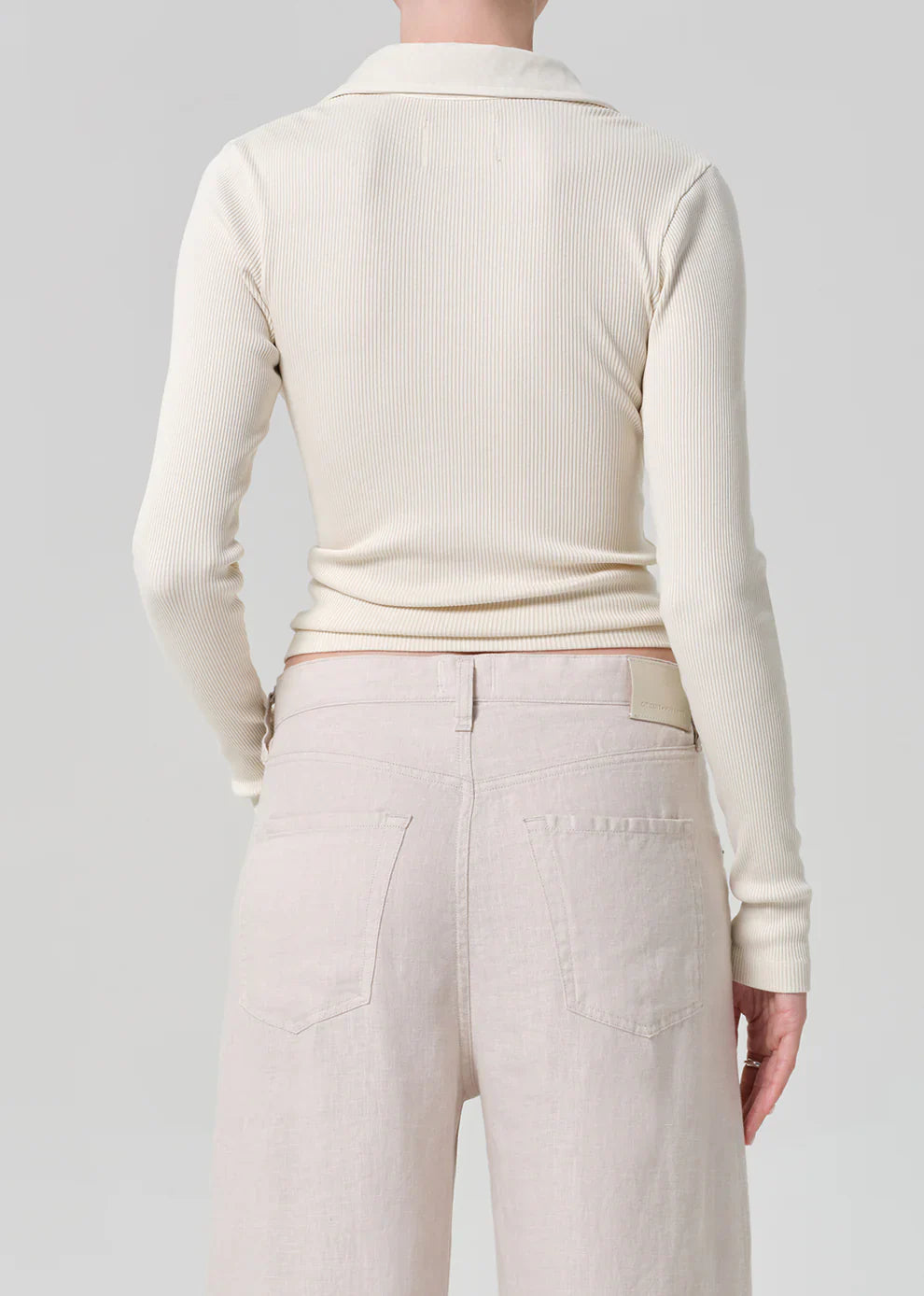 Person wearing a cream ribbed sweater and light-colored pants on a plain background