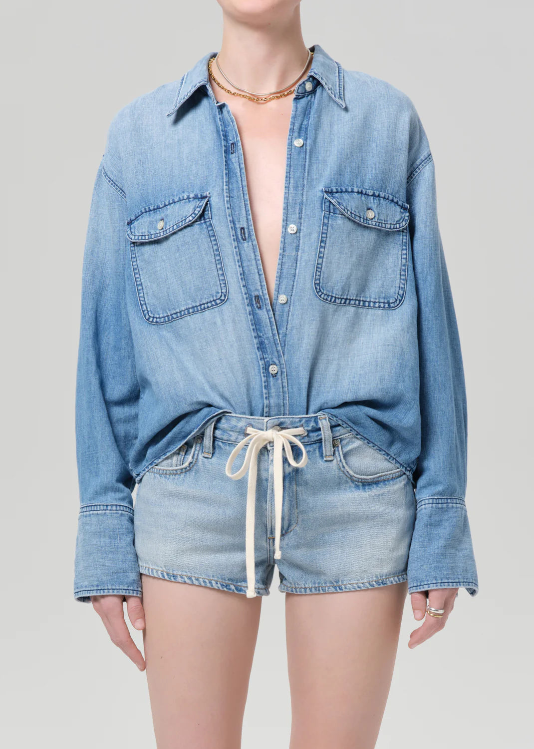 Person wearing a light blue denim shirt and shorts on a plain background