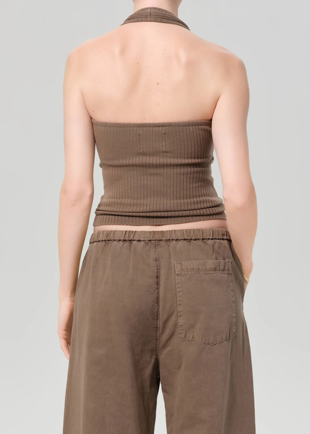 Person wearing a brown strapless top and pants on a gray background