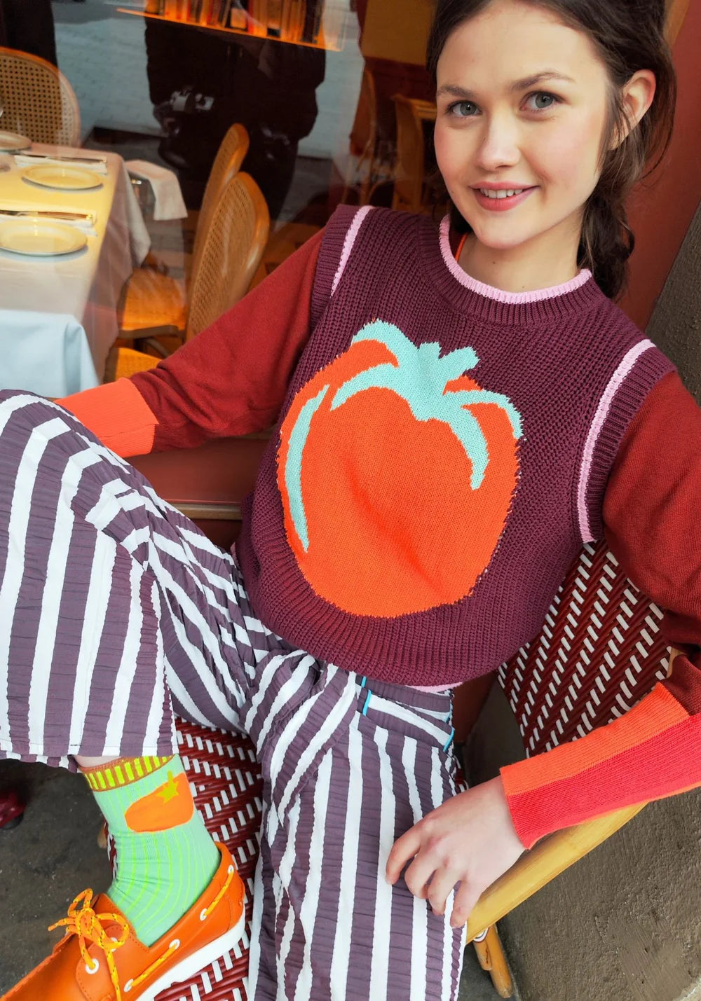 Woman wearing a sweater with a pumpkin design sitting outdoors.