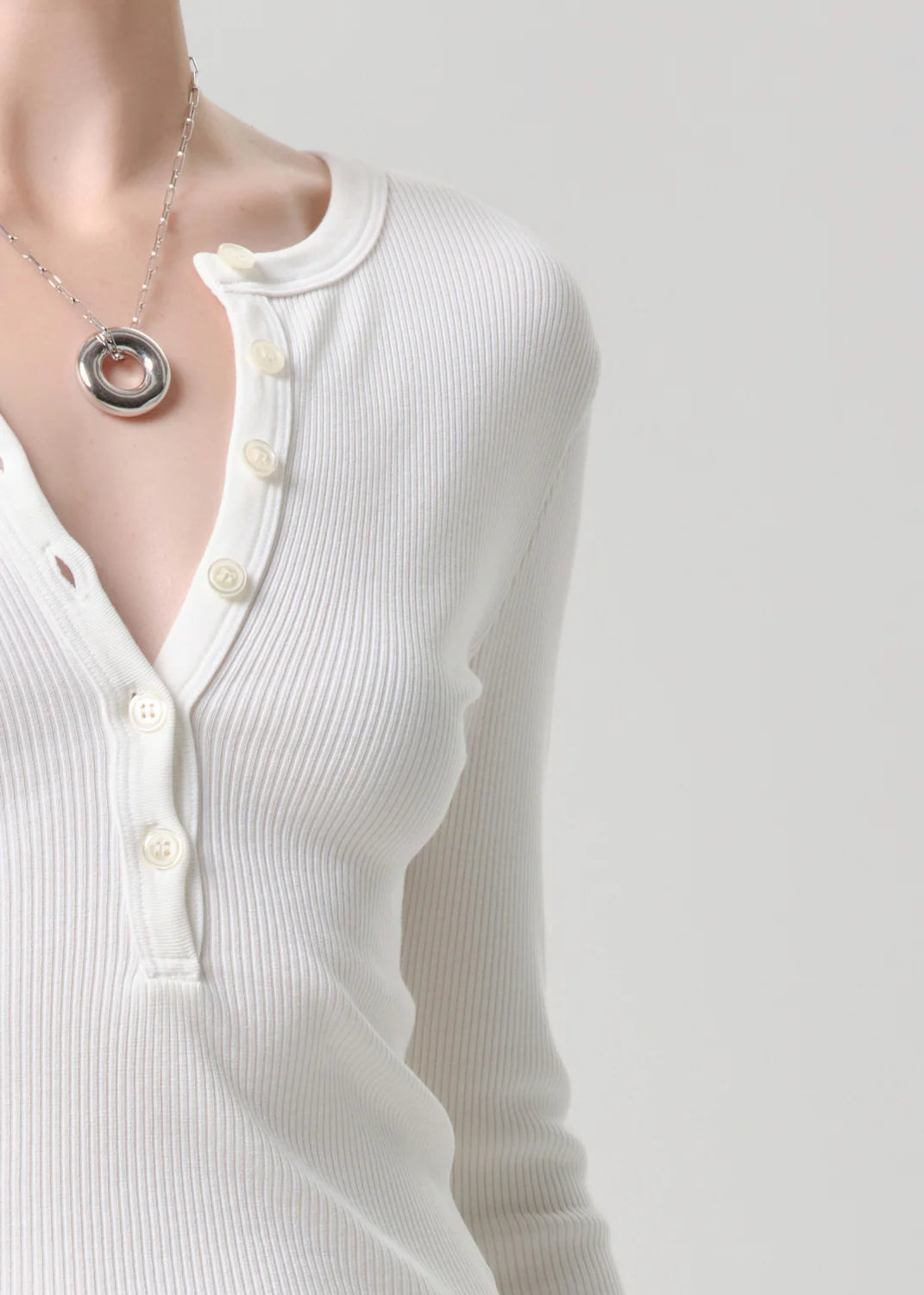 White ribbed sweater with buttons and a necklace on a plain background
