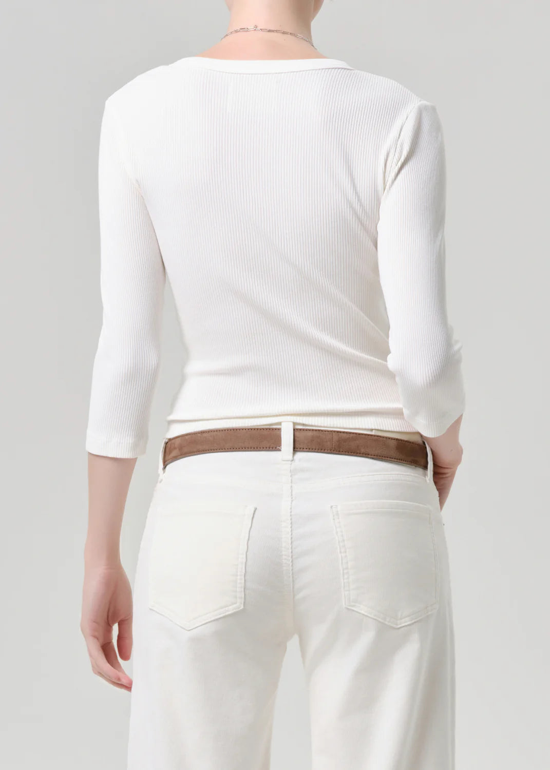 Person wearing a white long-sleeve top and white pants with a brown belt on a plain background