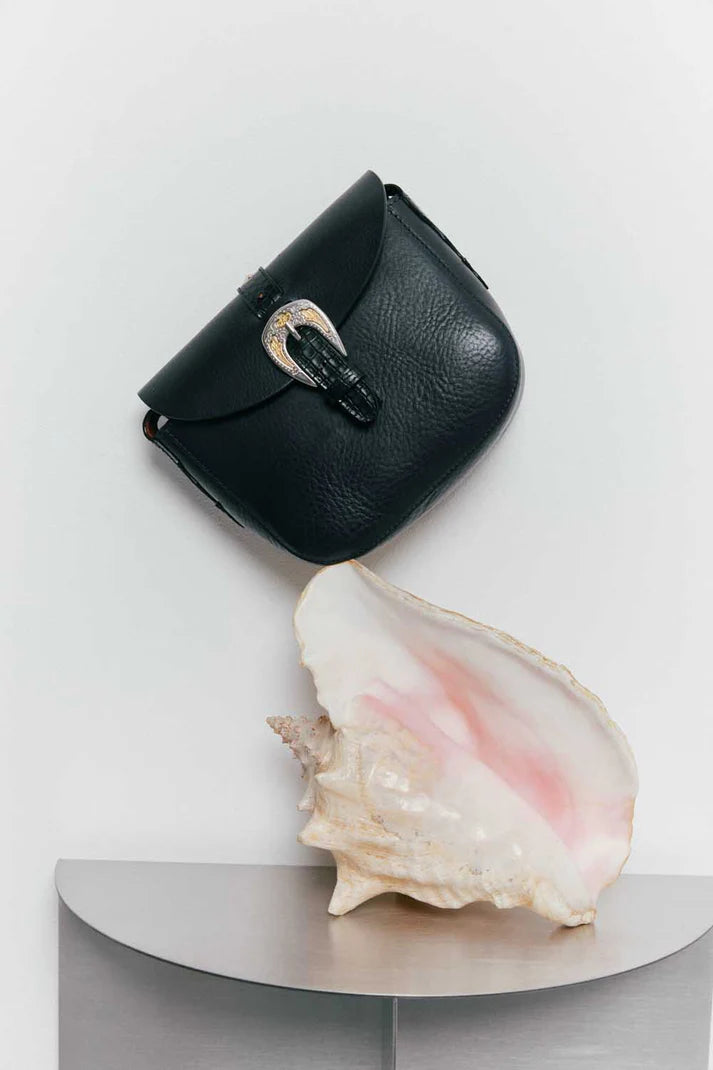 Black leather pouch with silver clasp next to a large shell on a white background