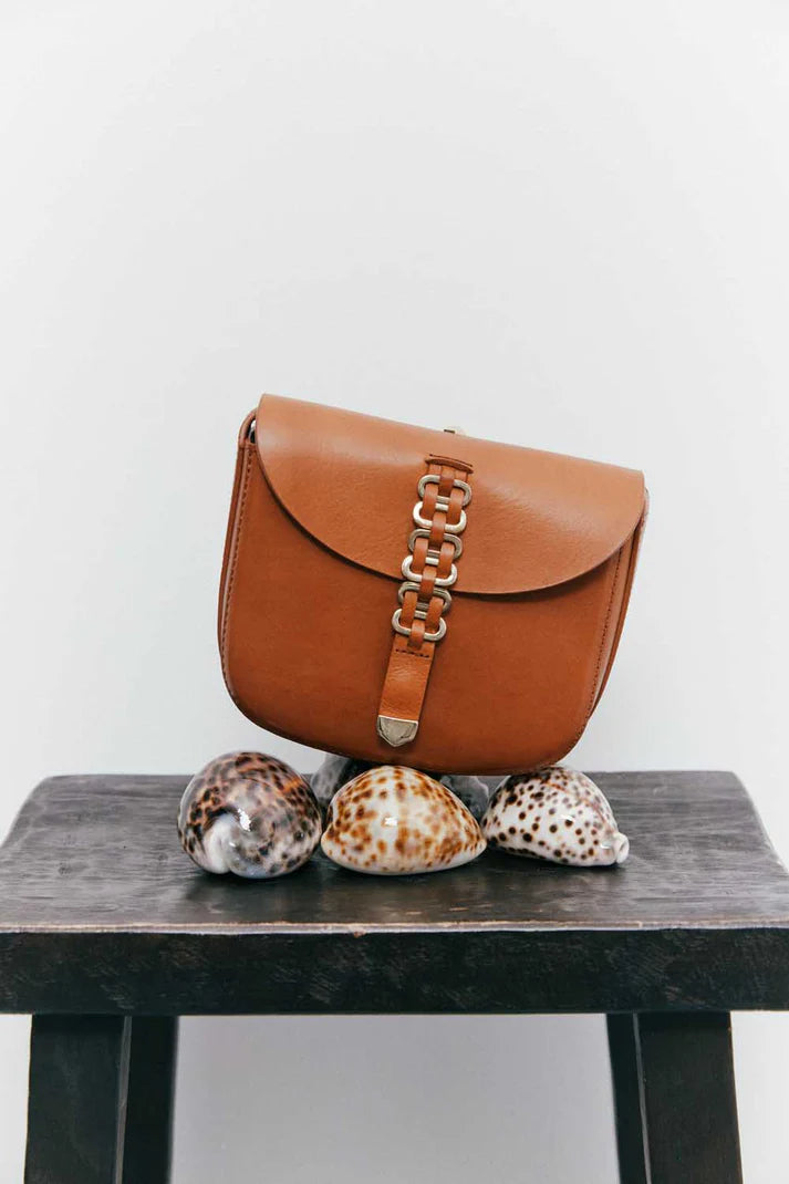Brown leather handbag with chain detail on a wooden surface with seashells.