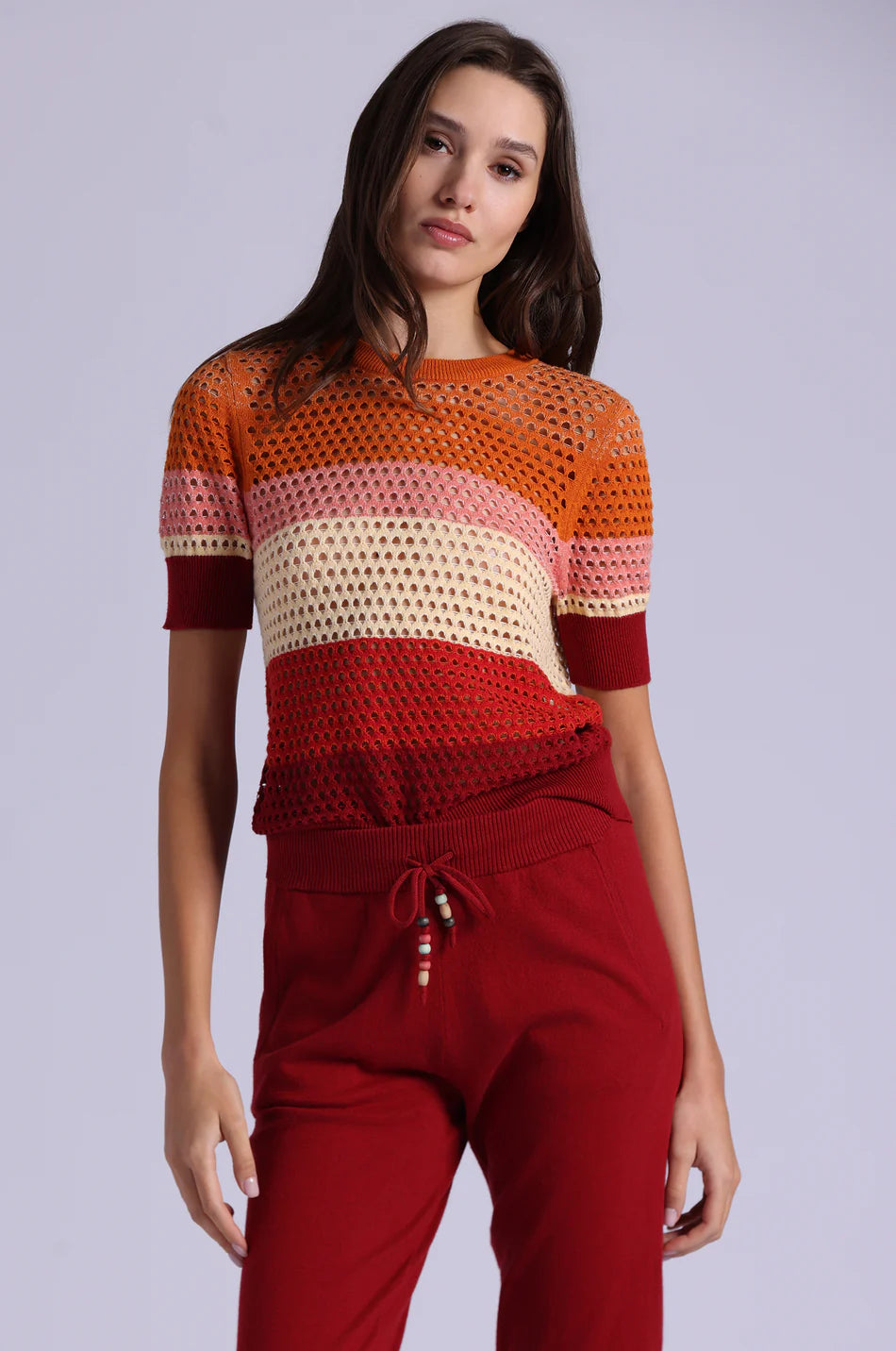 Woman wearing a colorful crochet top and red pants on a light gray background