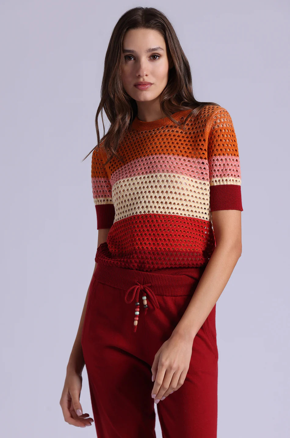 Woman wearing a colorful crochet top and red pants on a light gray background