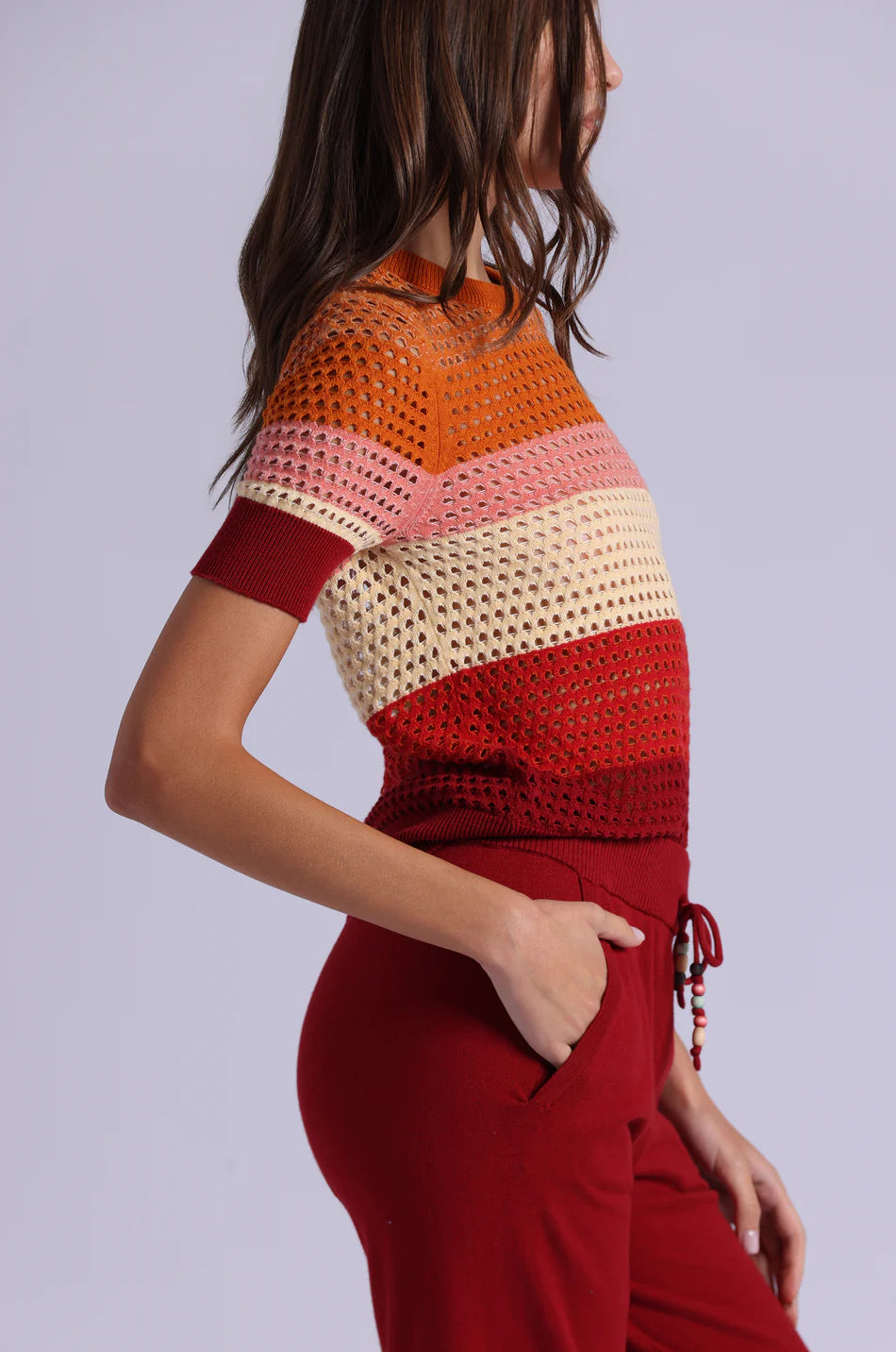 Woman wearing a colorful crochet top and red pants on a light gray background