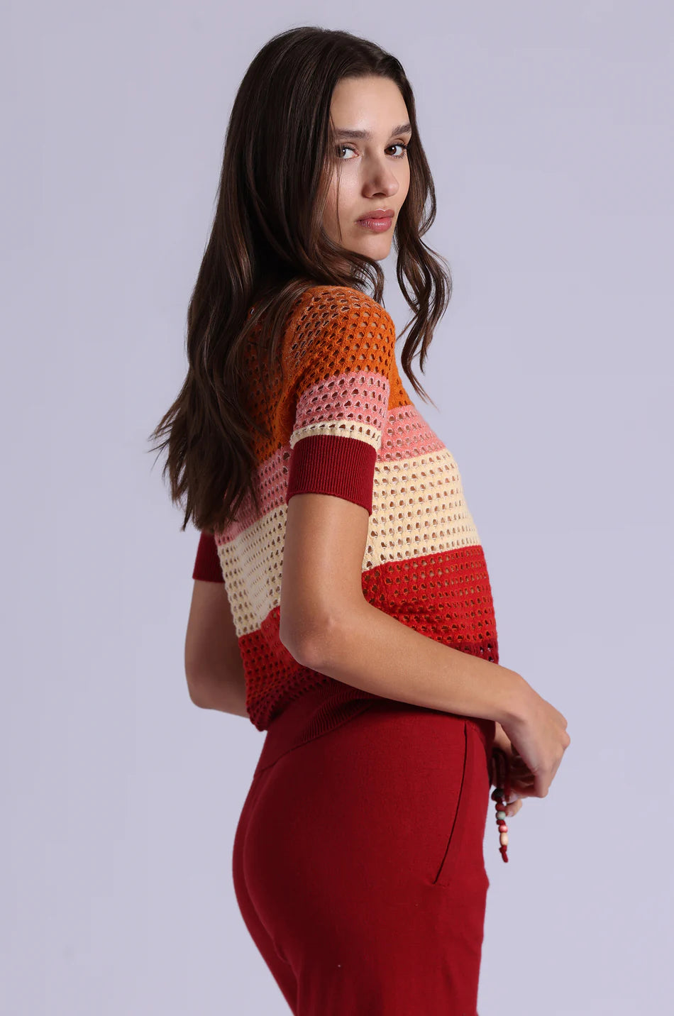 Woman wearing a colorful crochet top and red pants against a plain background