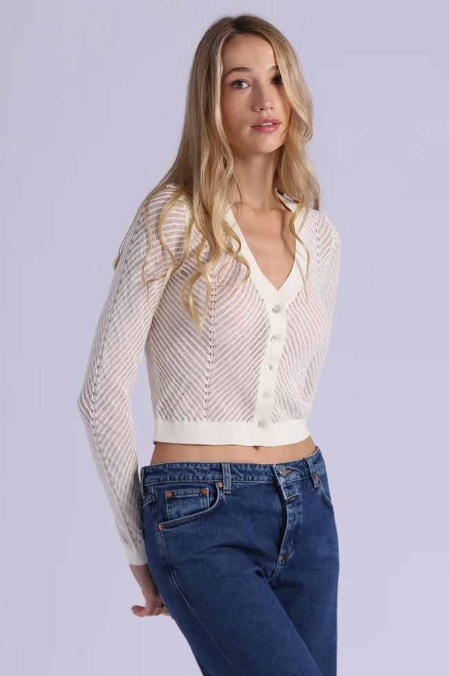 Woman wearing a white knit cardigan over a white shirt with blue jeans on a light gray background