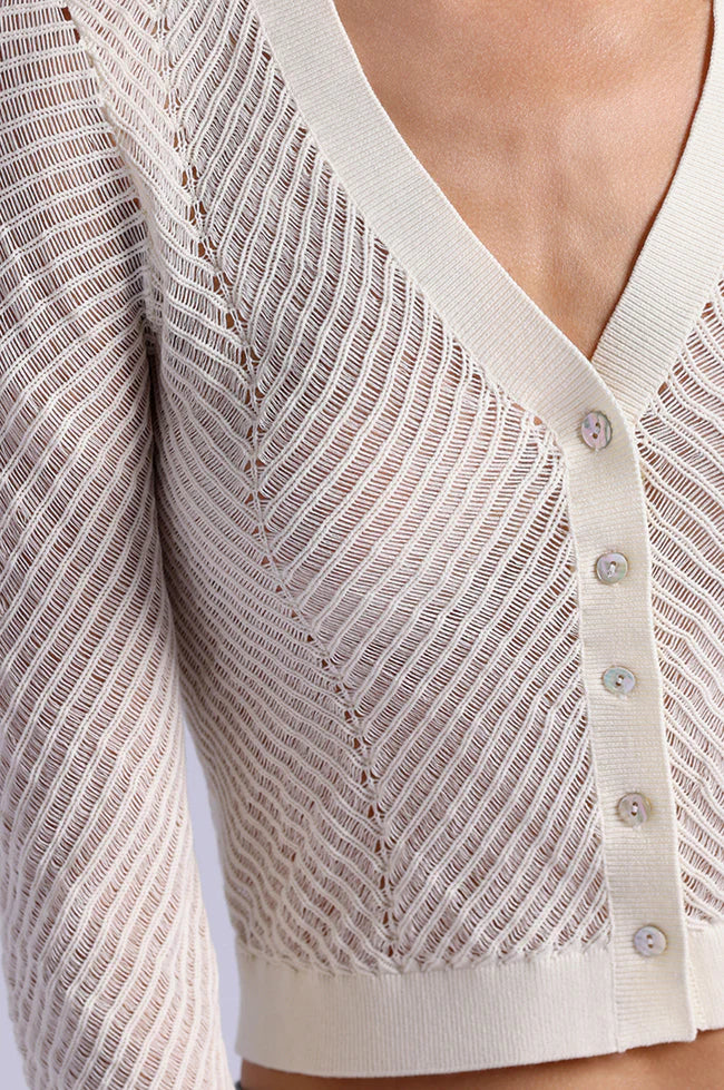 Close-up of a textured beige cardigan with buttons on a plain background