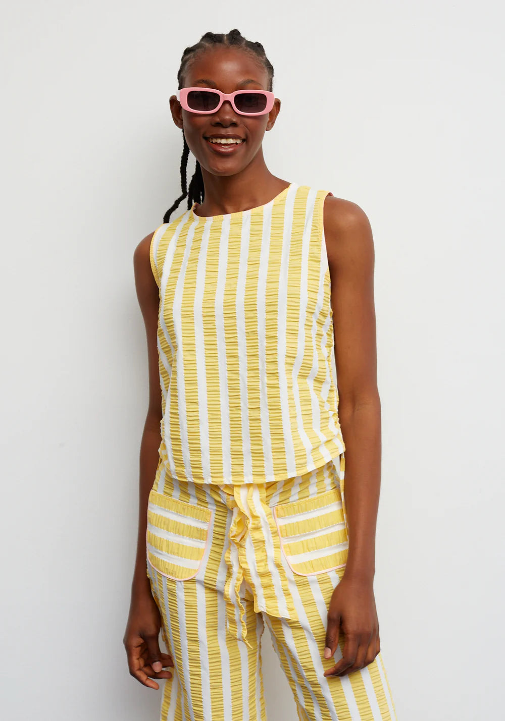 Woman wearing a yellow striped outfit with pink sunglasses against a white background